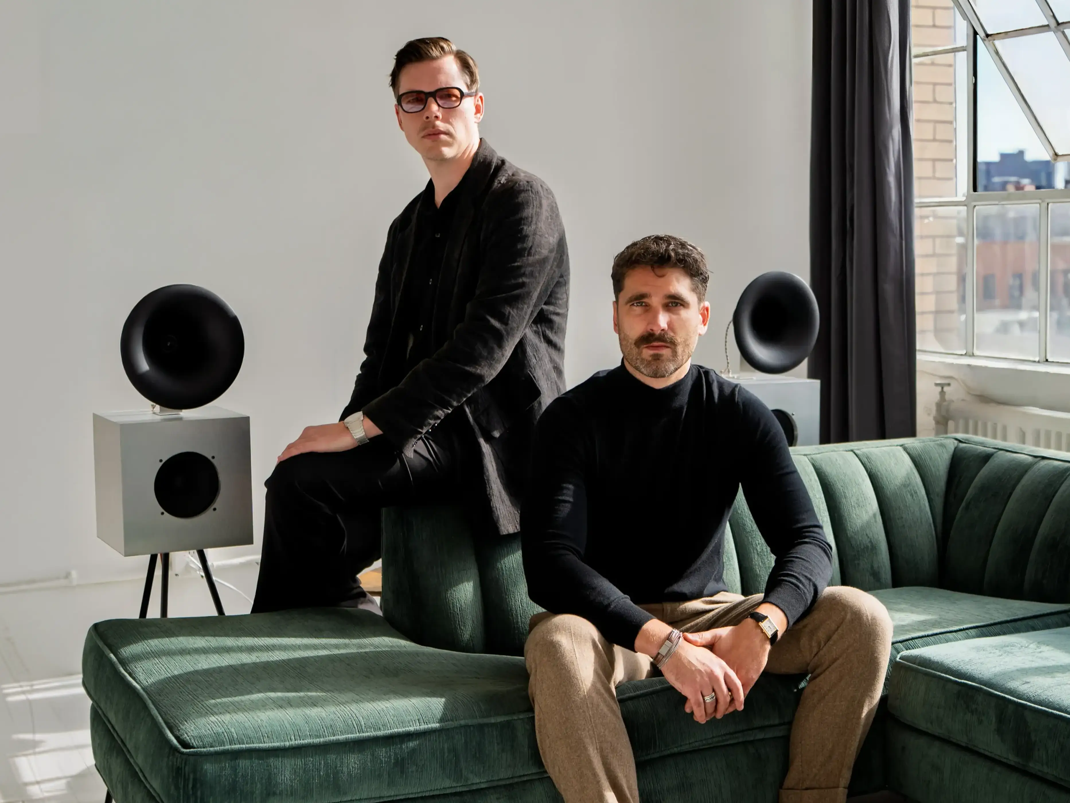 ATG cofounders Dillon Erb and Daniel Kobran, posed on a green couch in a studio with a white backdrop and an open window.