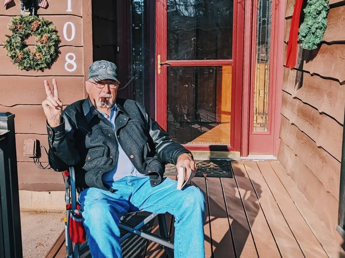 Older man sitting in chair holding up peace sign