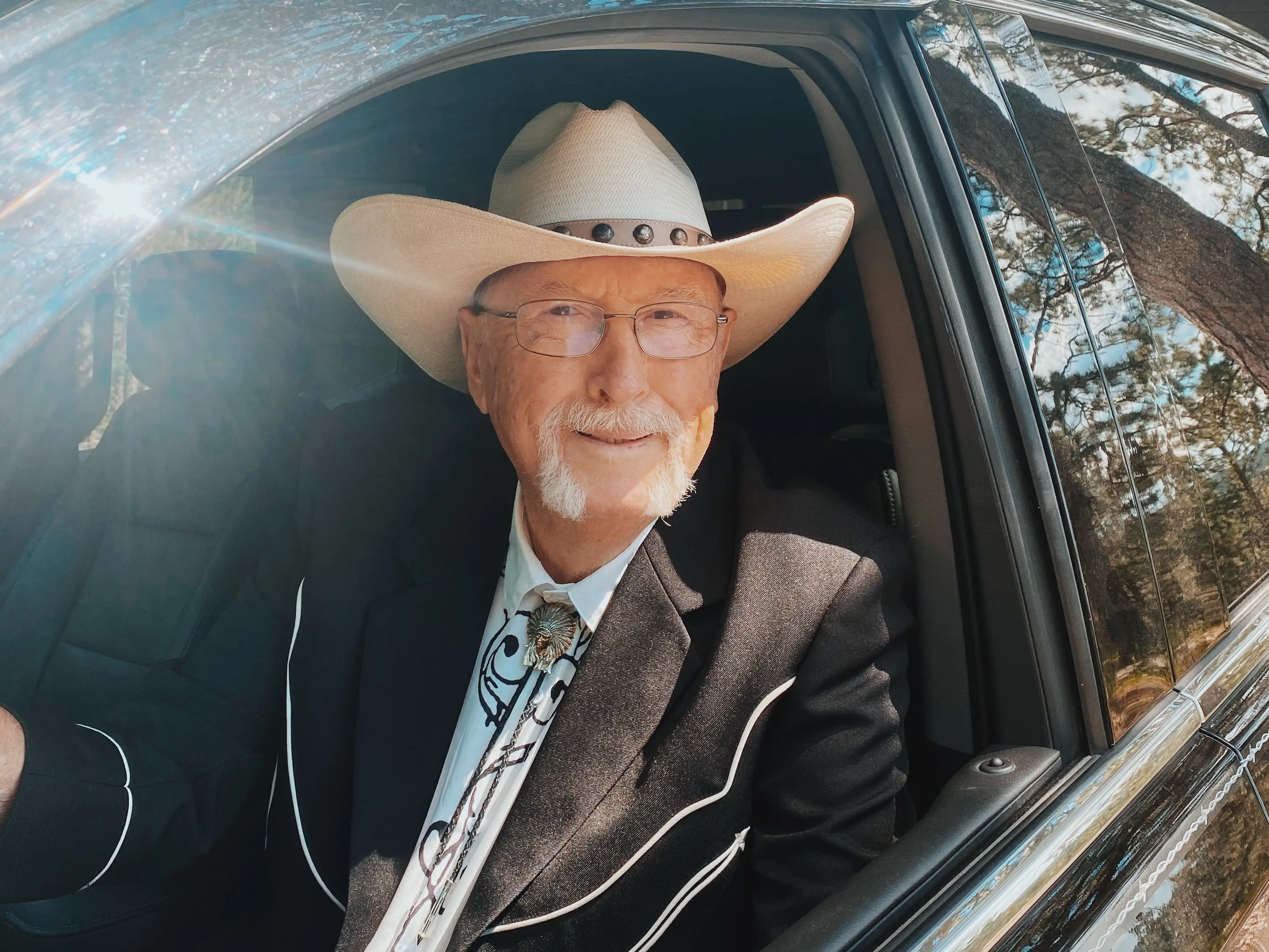 Older man in cowboy hat in driver's seat of car smiling