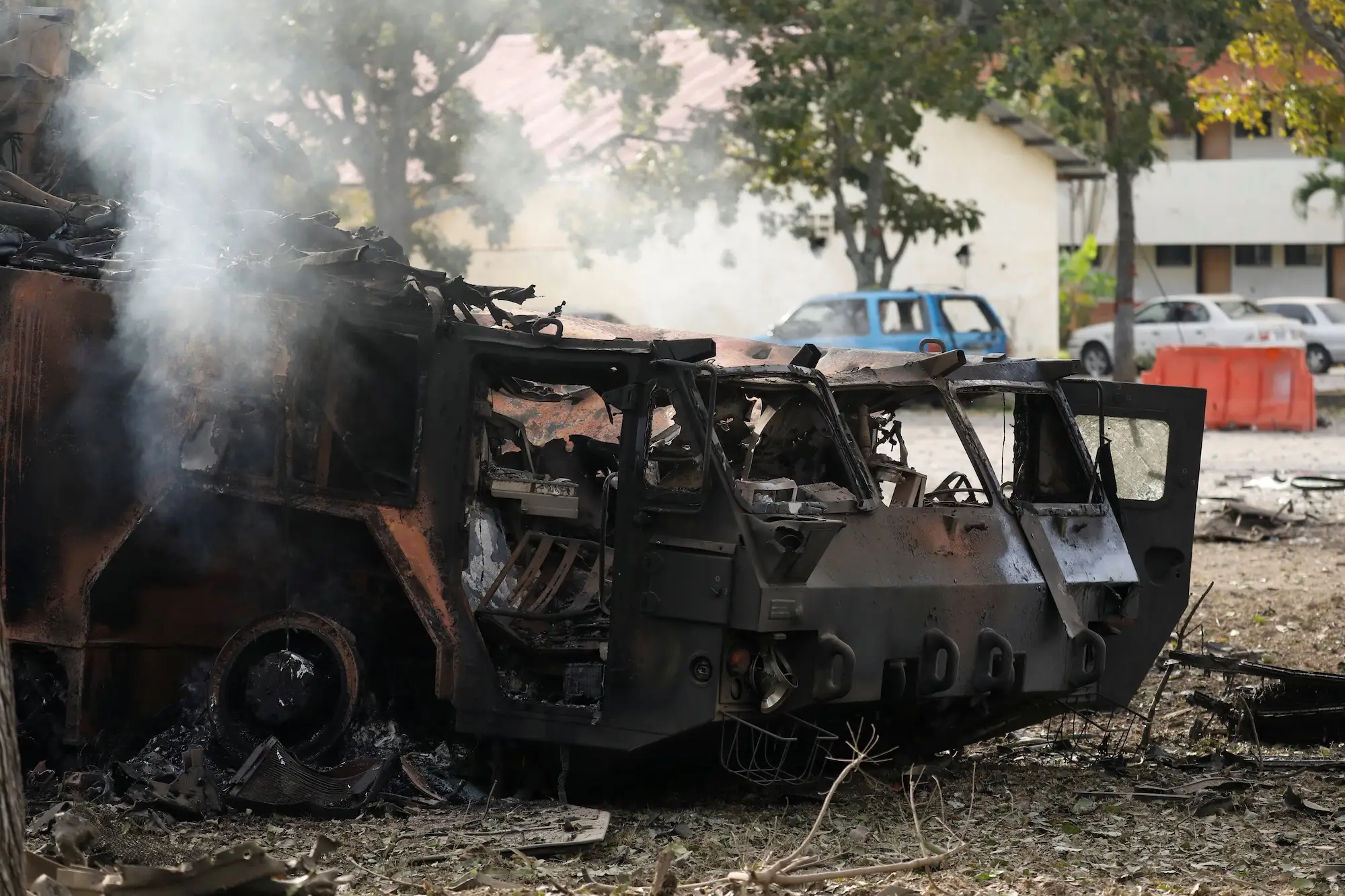 A blackened and charred piece of weaponry under some trees with some cars behind it