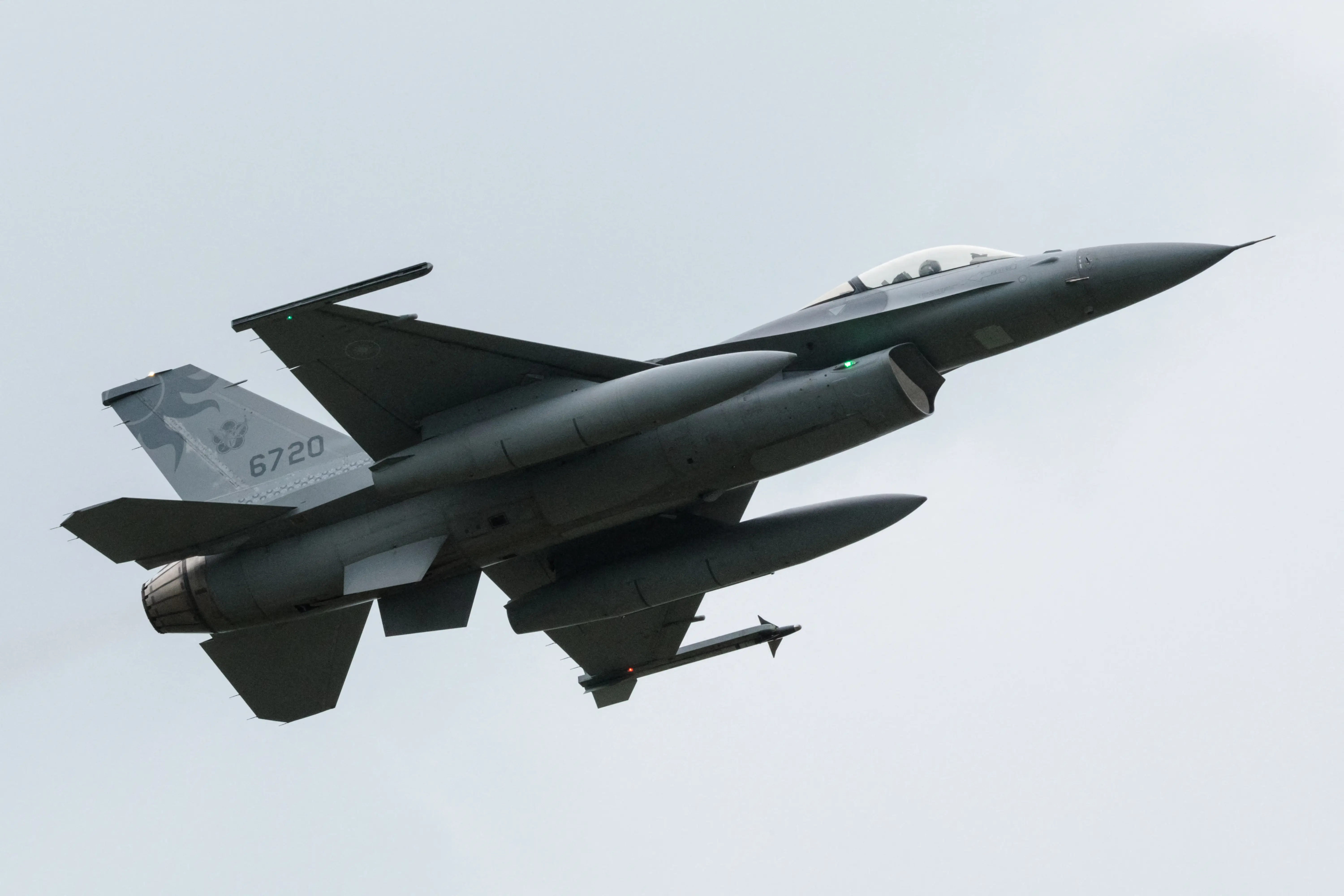 A Taiwanese F-16 is seen from the bottom right as it flies against a grey background.