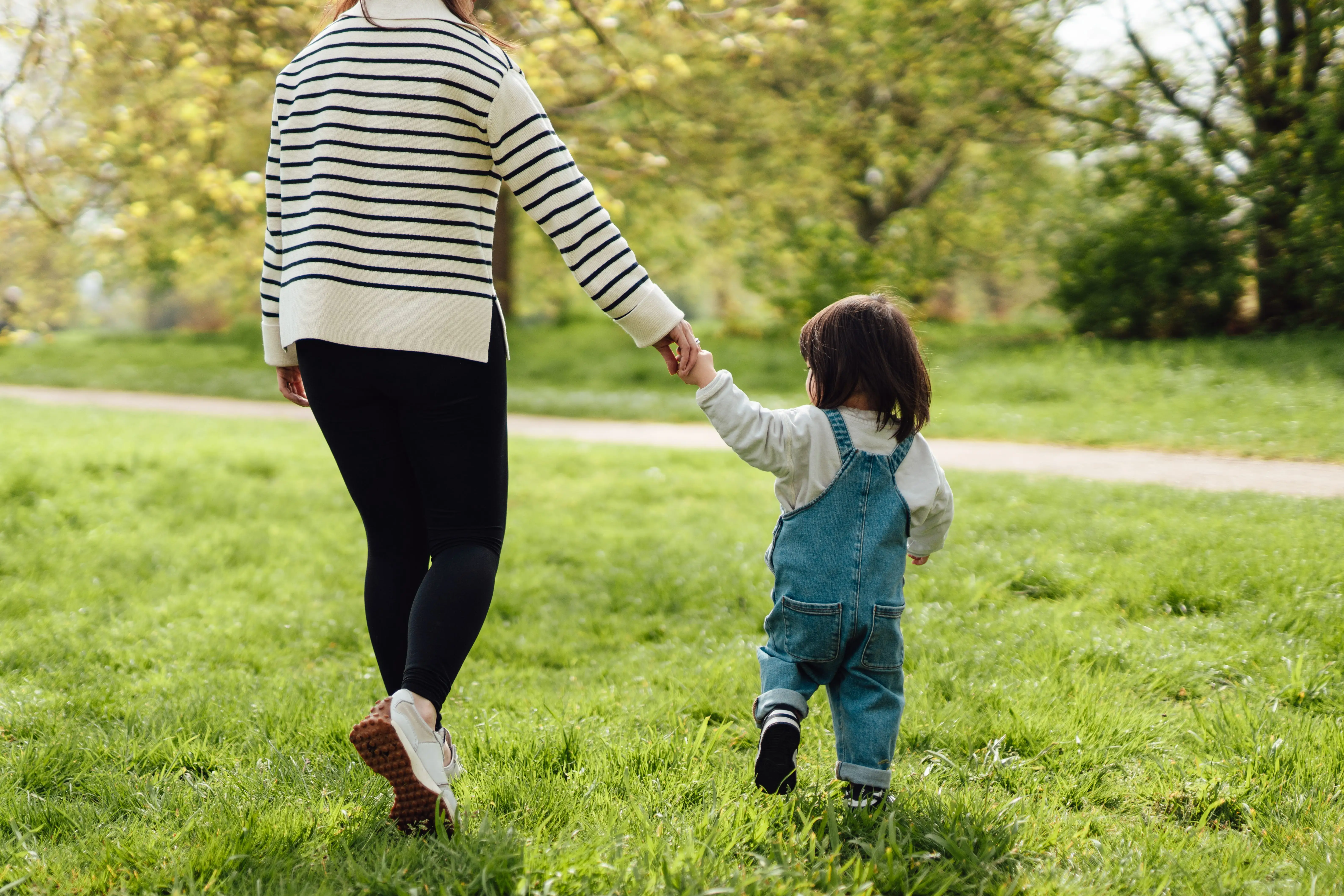 A mother and child walk in a park.