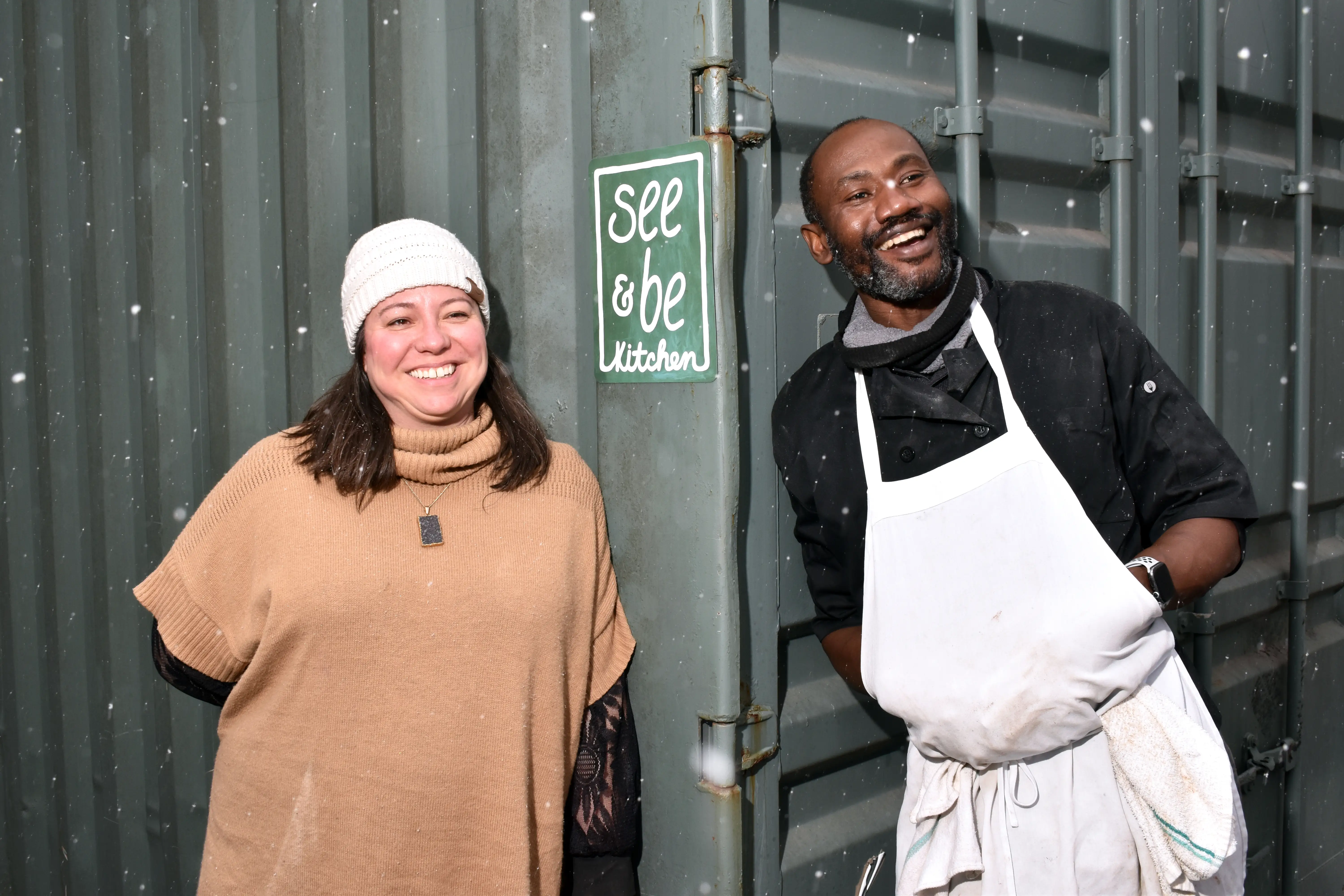 A man and a woman posing outside of a shipping container.