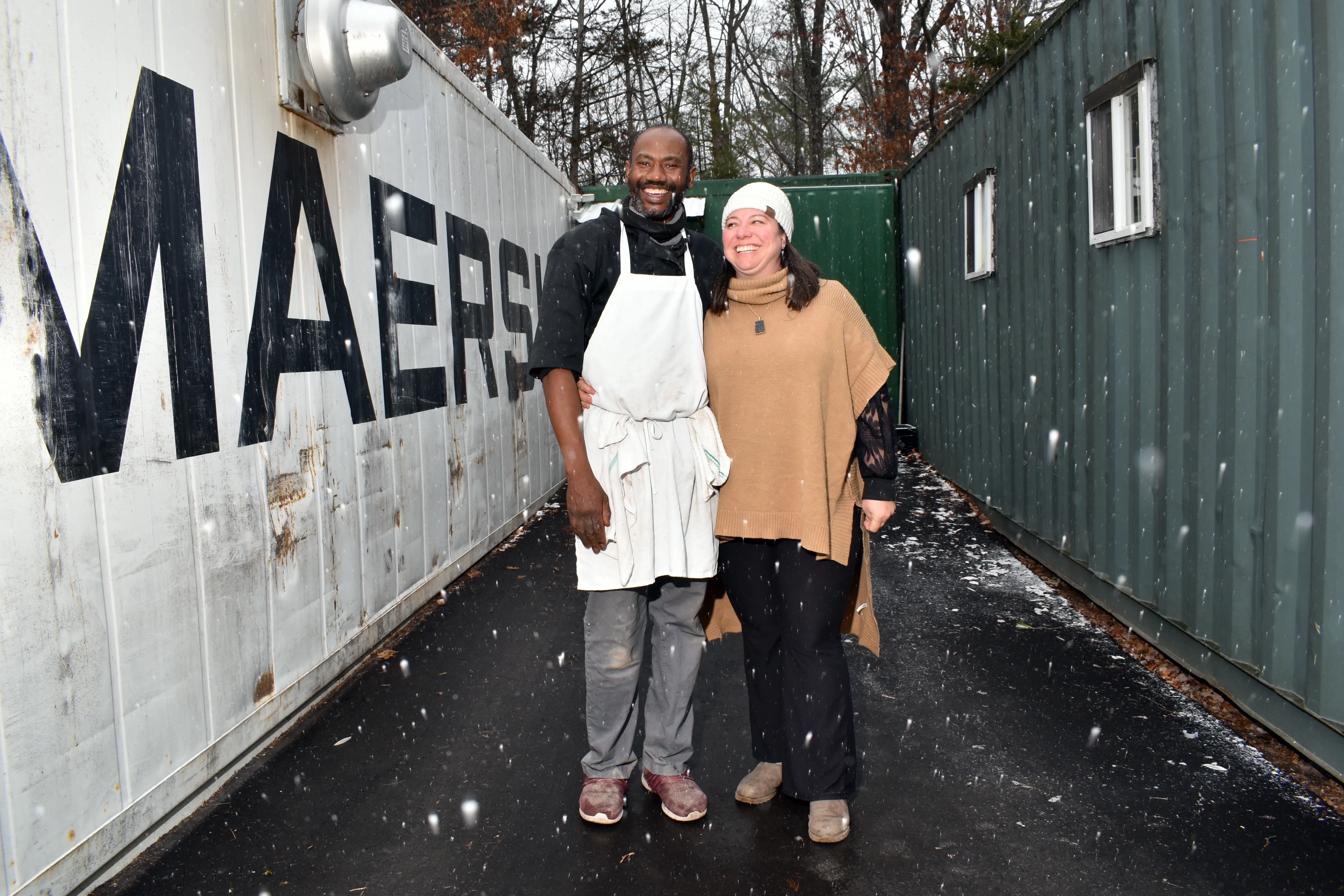 A man and a woman posing outside of shipping containers.