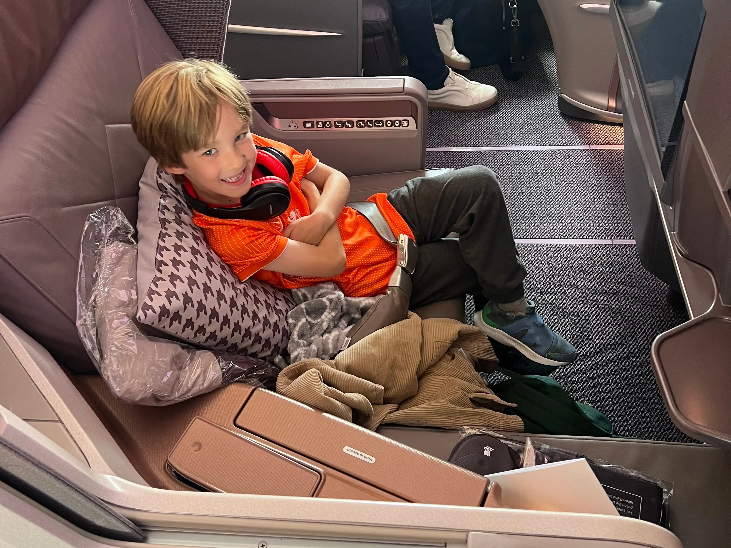 Child smiling with pillows, blanket in Business class seat on Singapore airlines