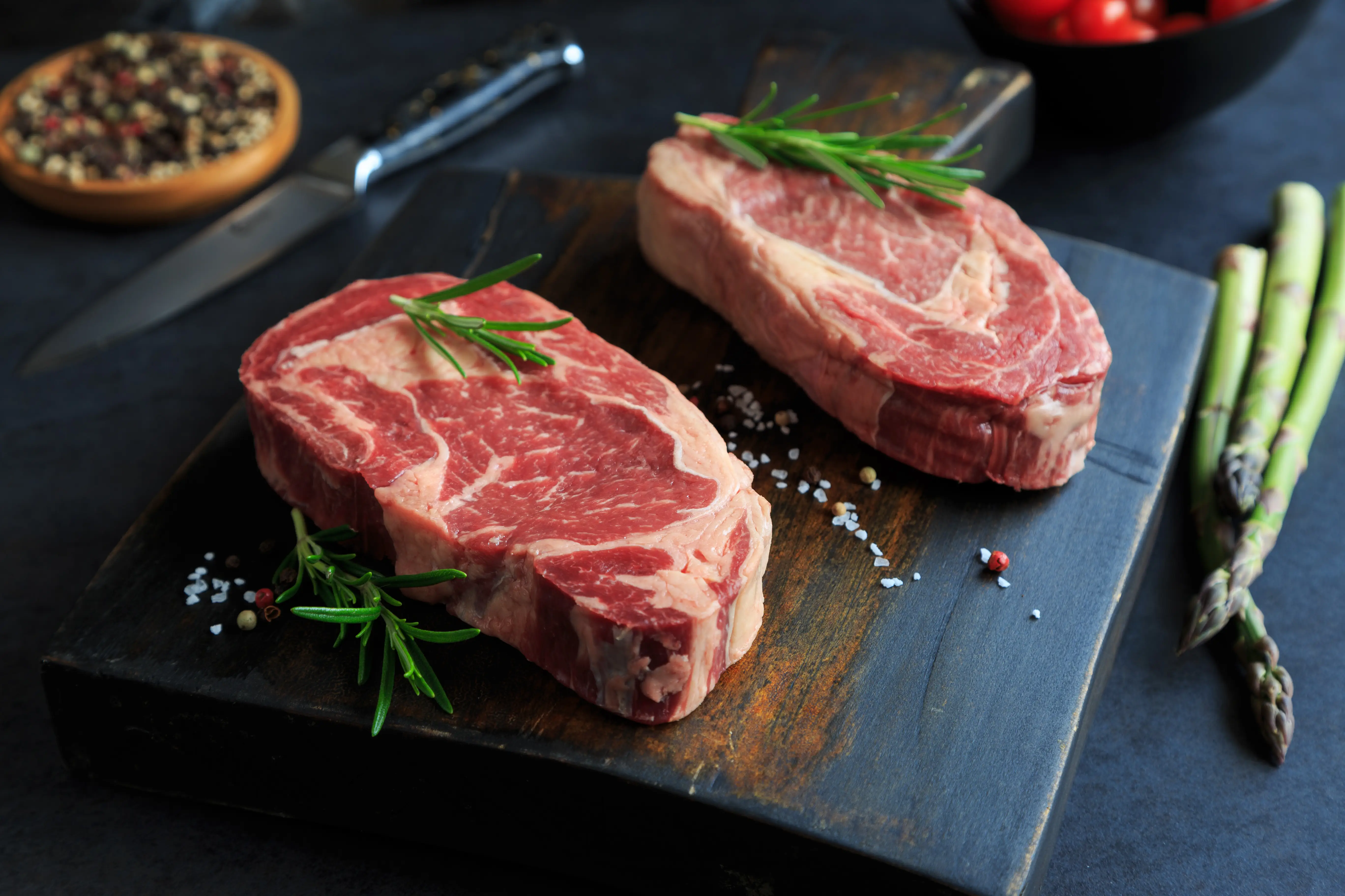 a close-up of thick steaks on a cutting board with a few asparagus spears