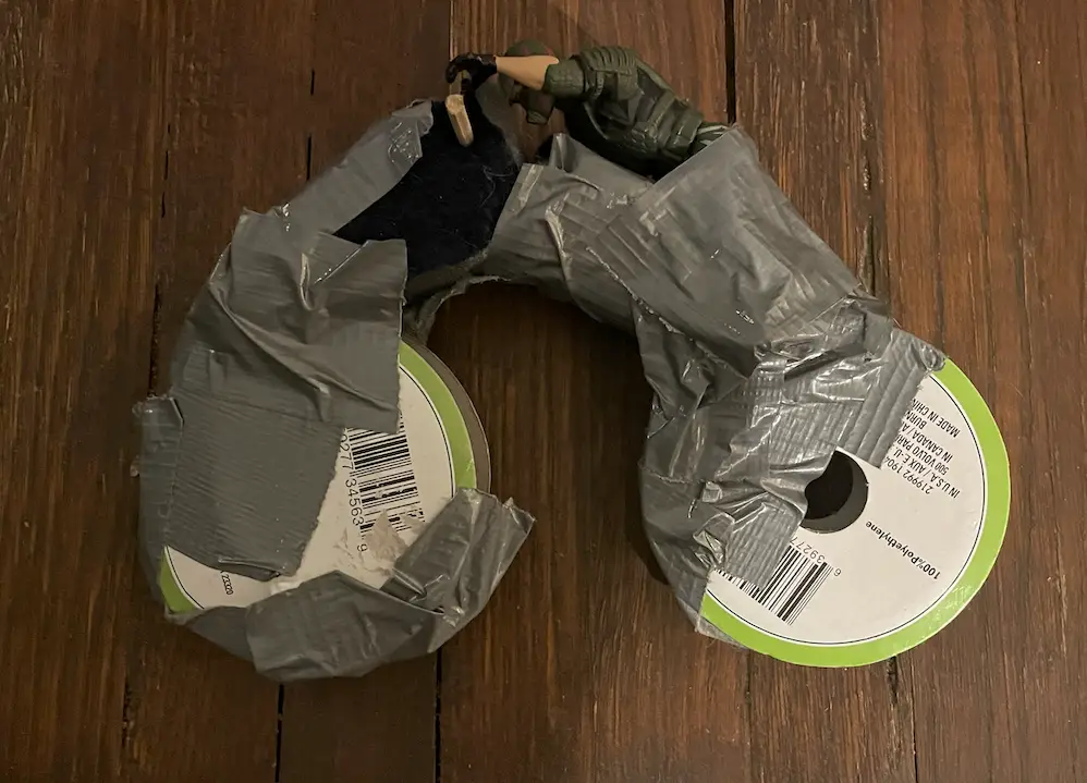 Two rolls of ribbon taped together with an action figure on top.