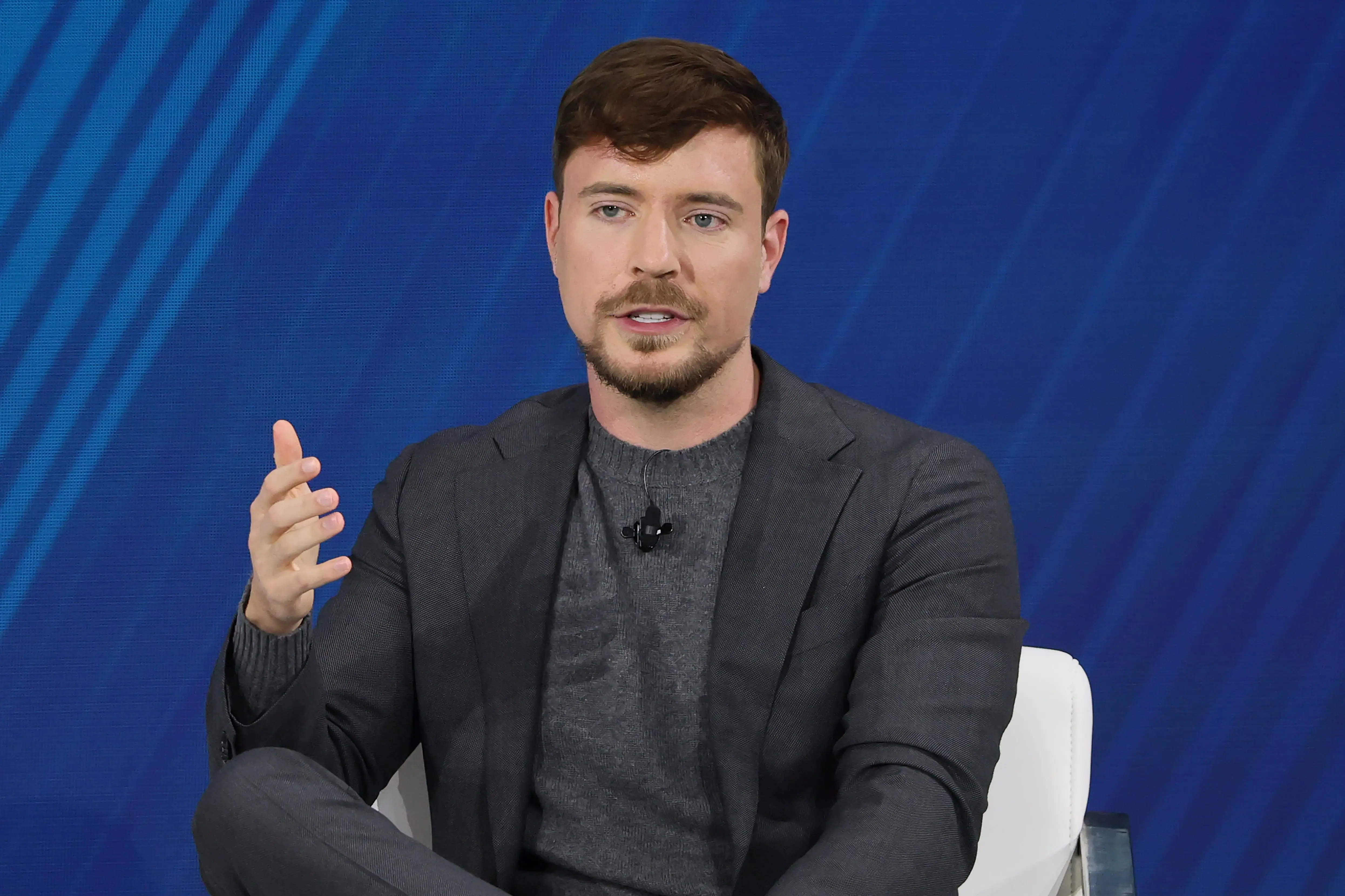 Jimmy Donaldson sitting on a white chair, wearing a gray suit.