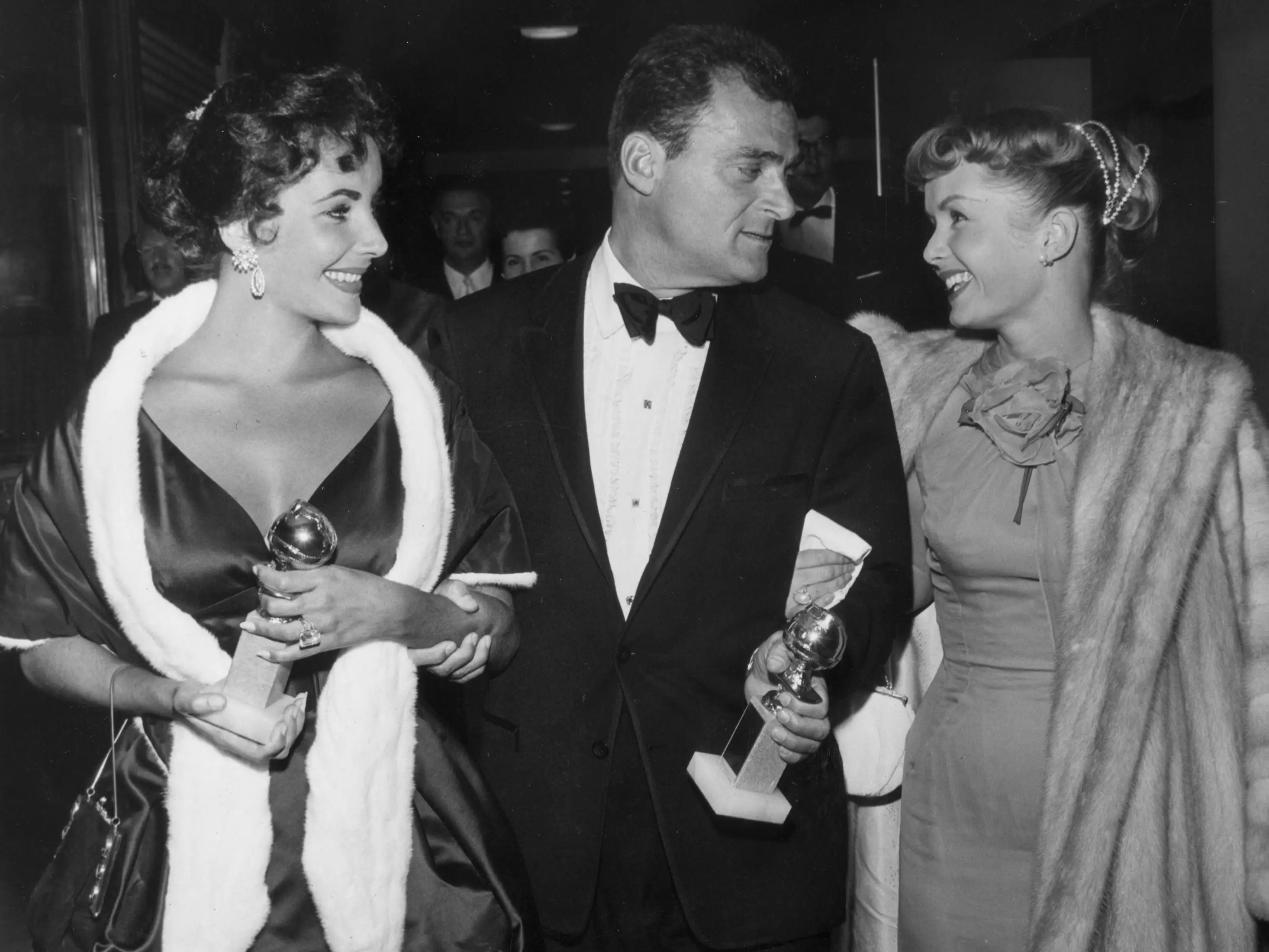 British-born actor Elizabeth Taylor and her husband, film producer Mike Todd (1909 - 1958), hold their Golden Globe awards while walking with American actor Debbie Reynolds