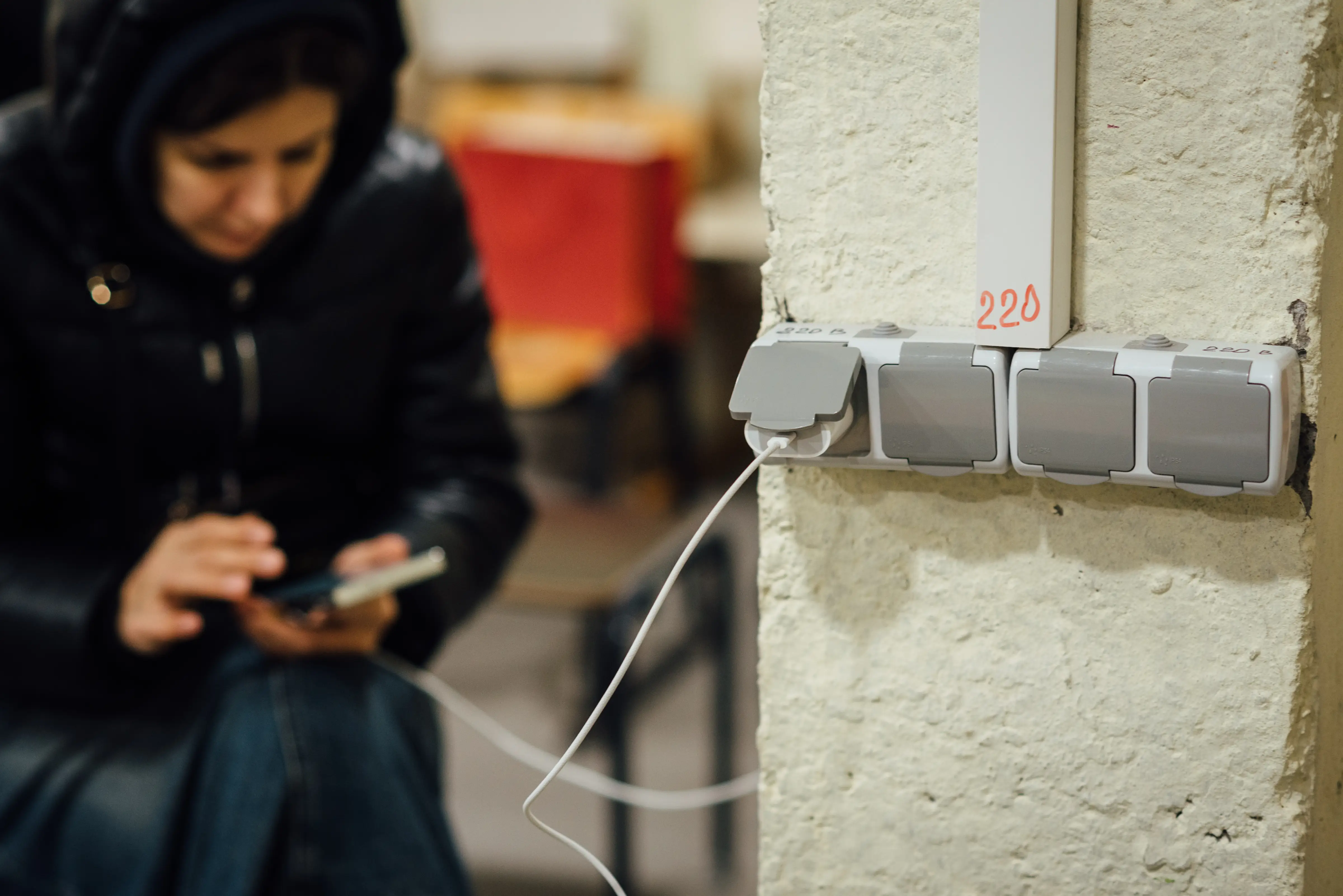A woman charges her smartphone at a wall plug.