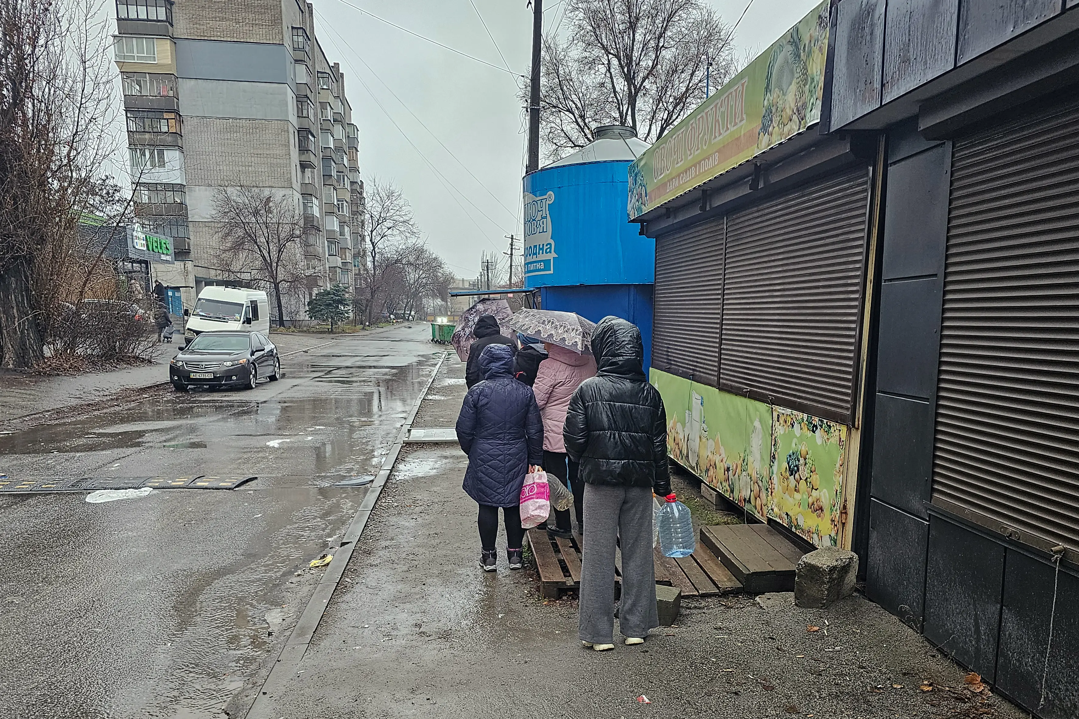Ukrainian residents queue up for water with plastic bottles on the street.