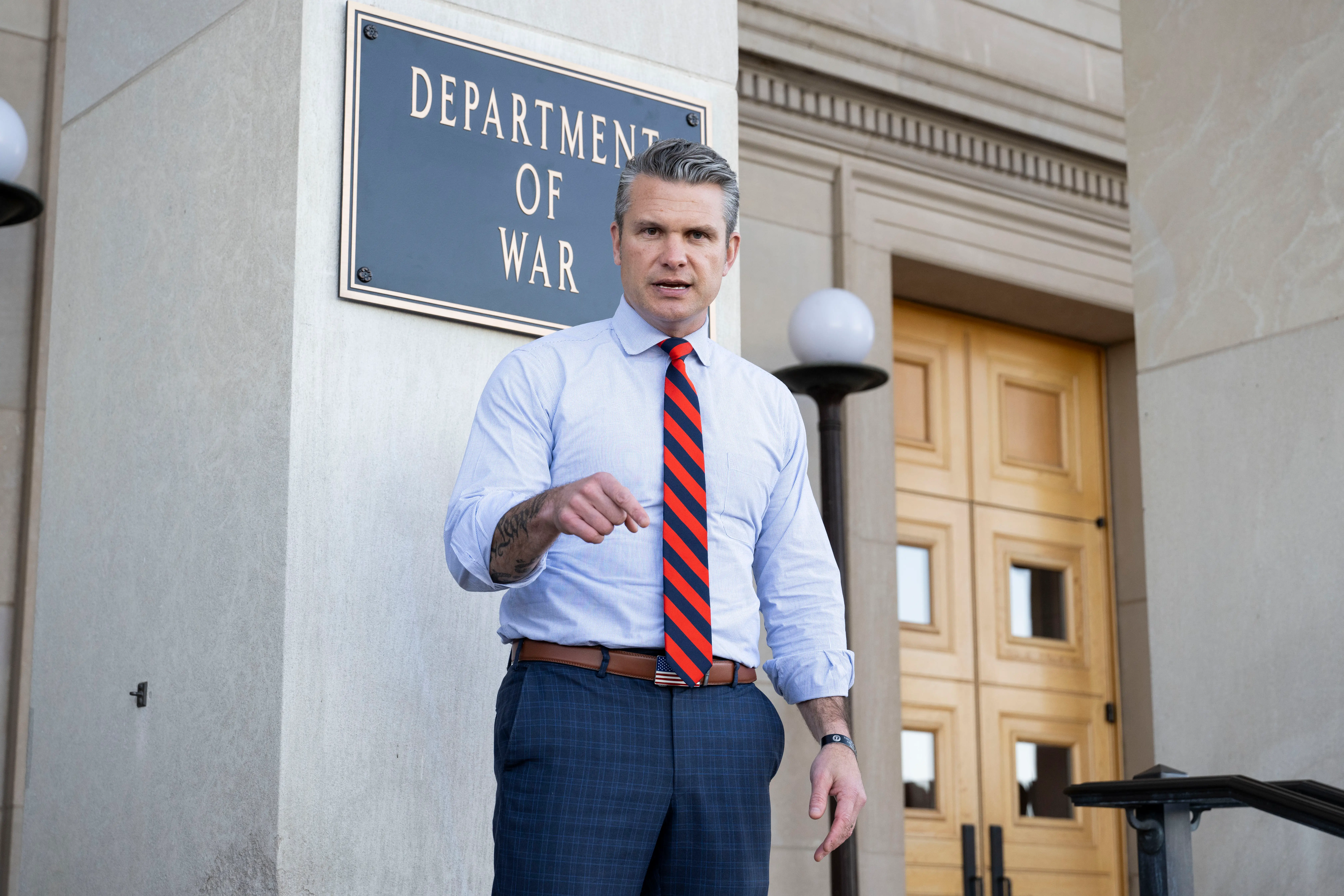Secretary of Defense Pete Hegseth standing in front of a Department of War sign