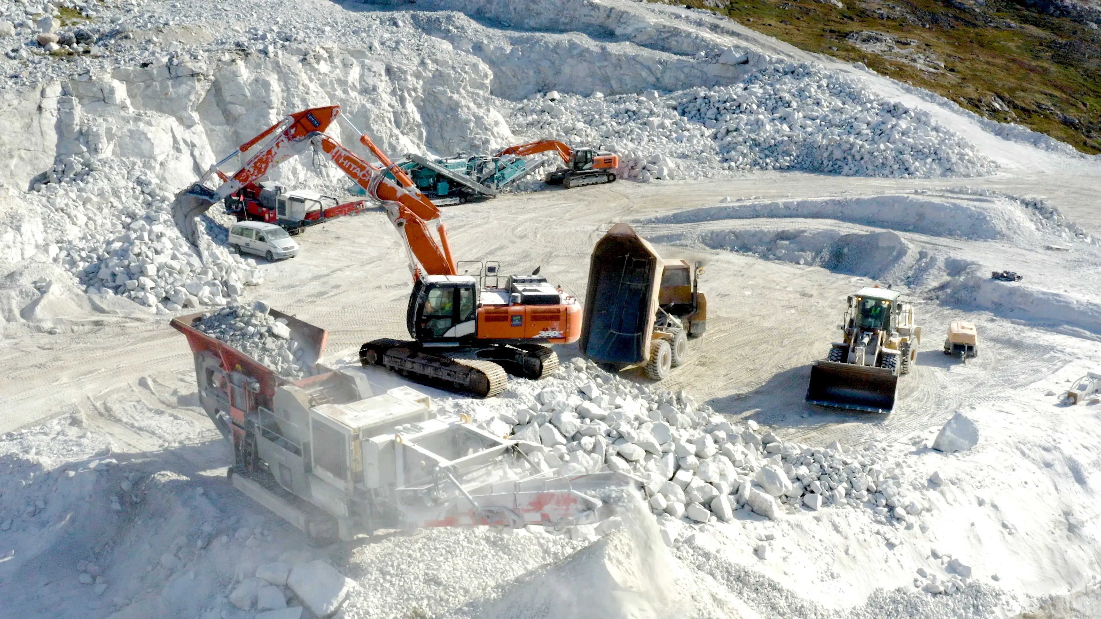 Orange construction machine mines white rocks, anorthosite, at Lumina mine in Greenland.
