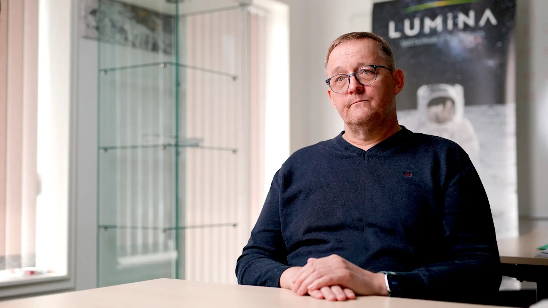 Bent Olvig in a blue shirt and glasses with Lumina poster in the background.