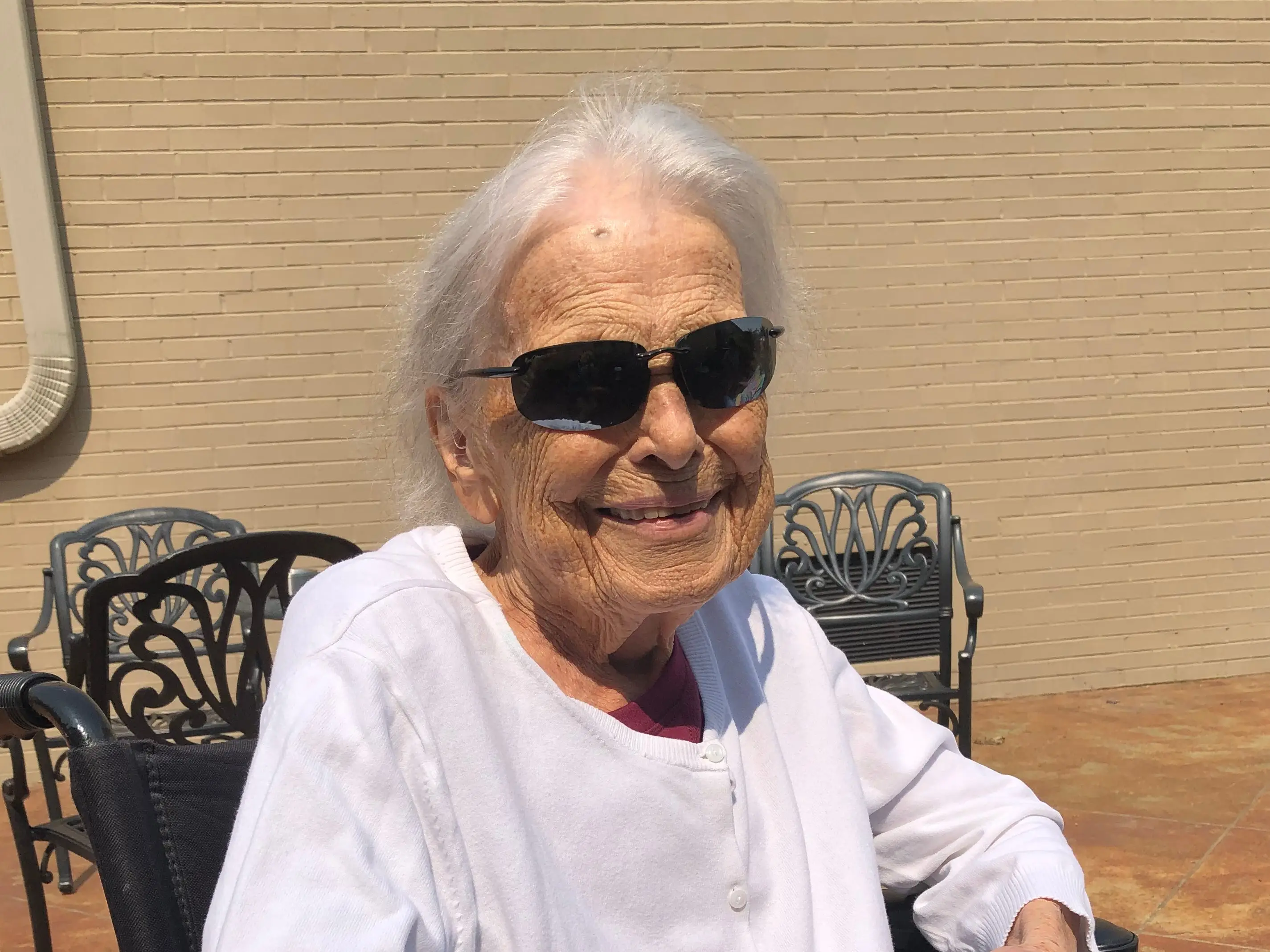 The author's grandmother smiling and wearing sunglasses while sitting outside.