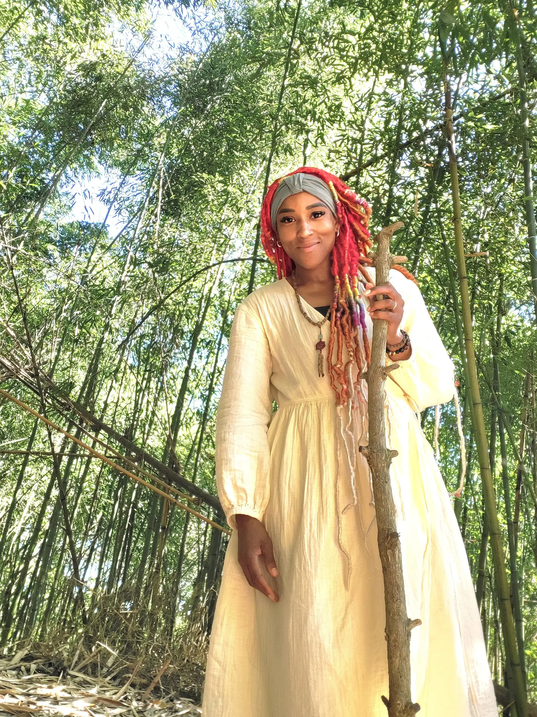 A woman posing in the forest with a large stick.