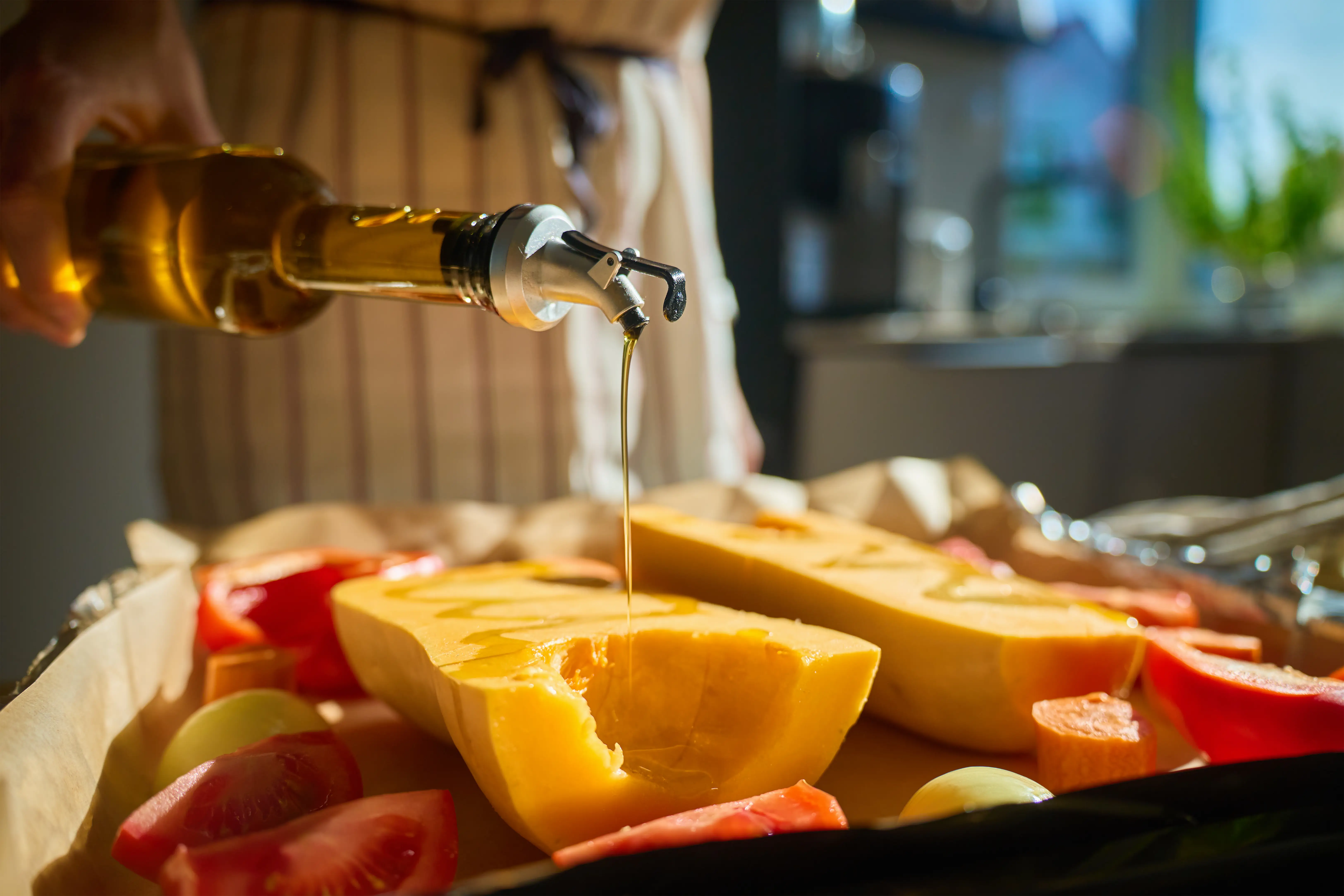 A home cook drizzles olive oil over a tray of vegetables.