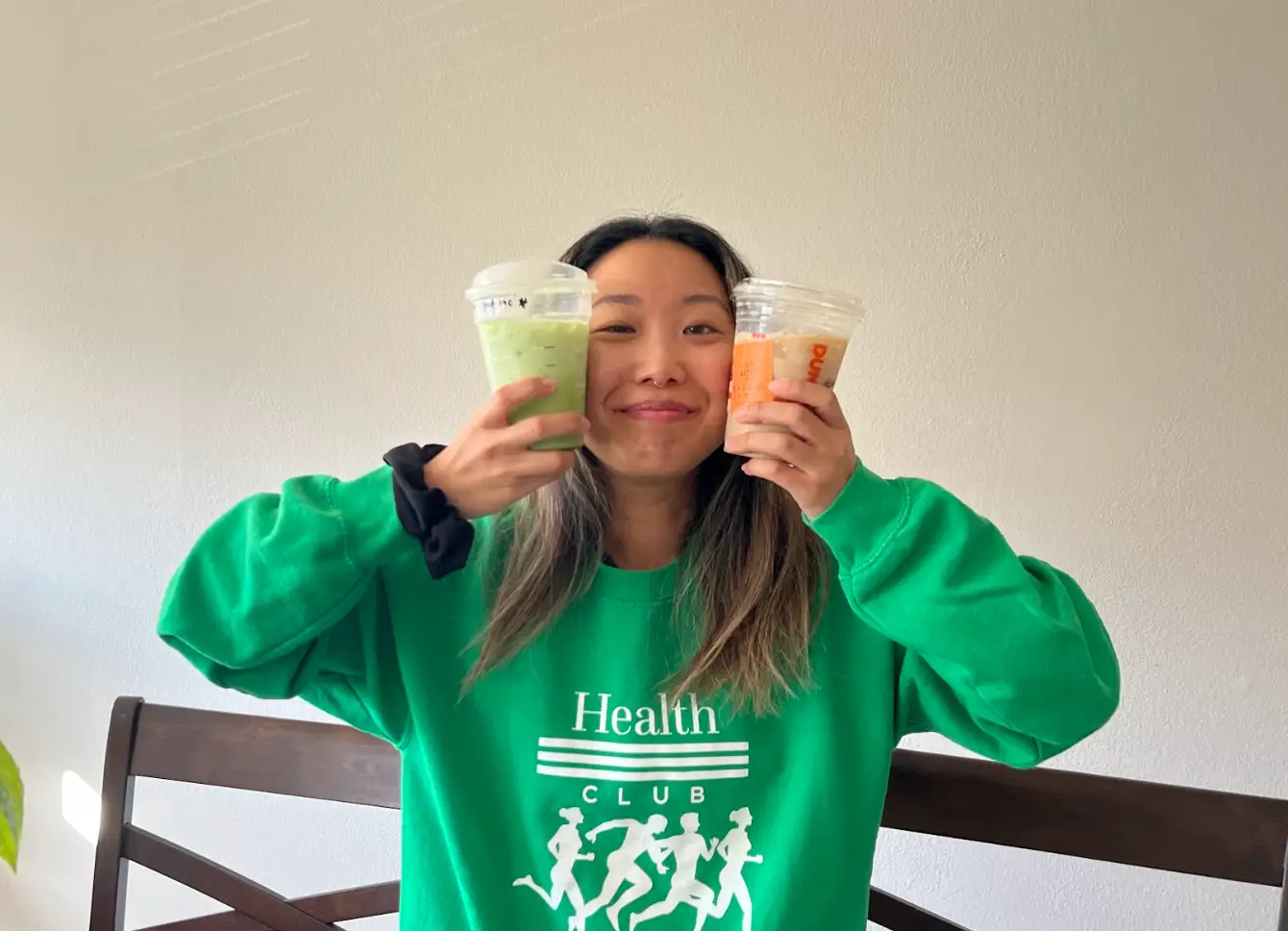 The writer holding up a protein drink from Starbucks in one hand, and a protein drink from Dunkin' in the other.