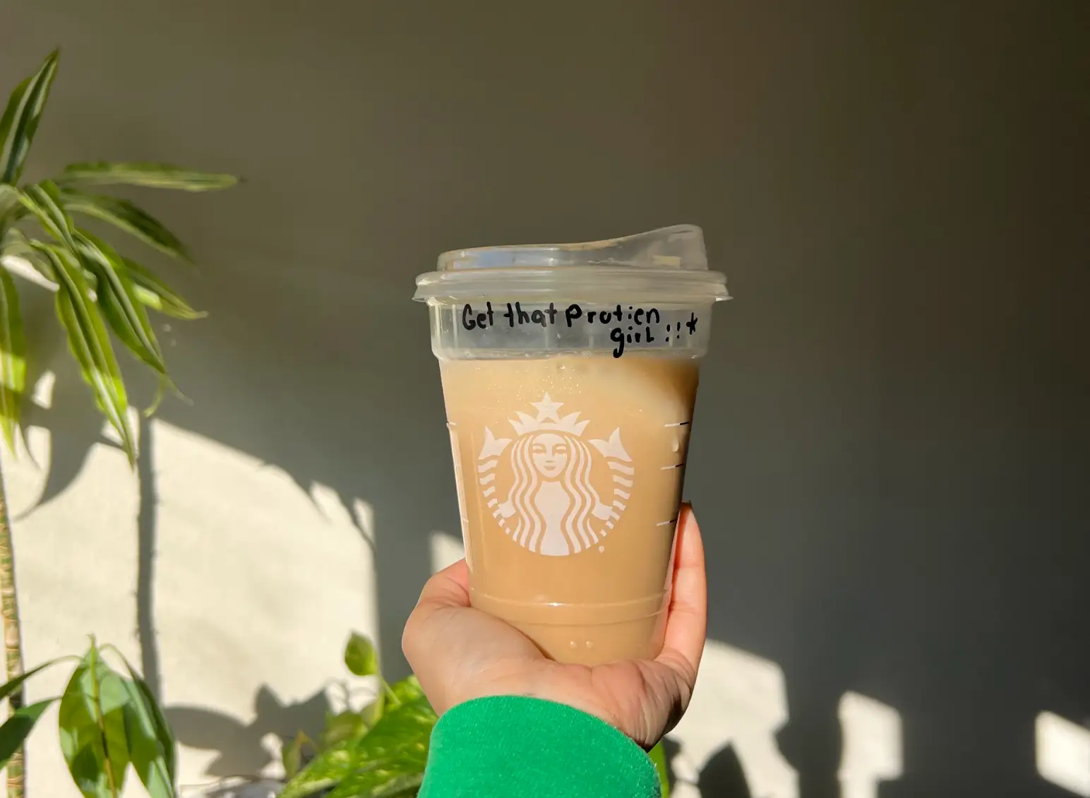 The writer holding up an iced caramel protein latte from Starbucks.