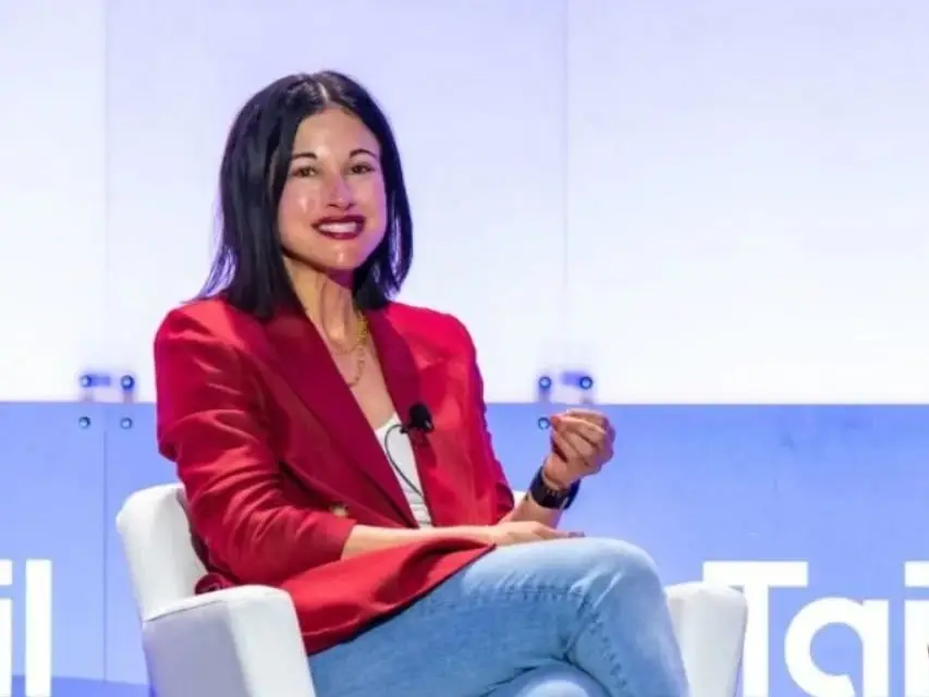 a woman speaks on a stage in a red blazer