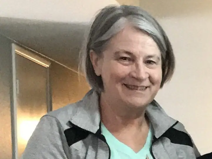 A woman wearing a blue top and a gray jacket.