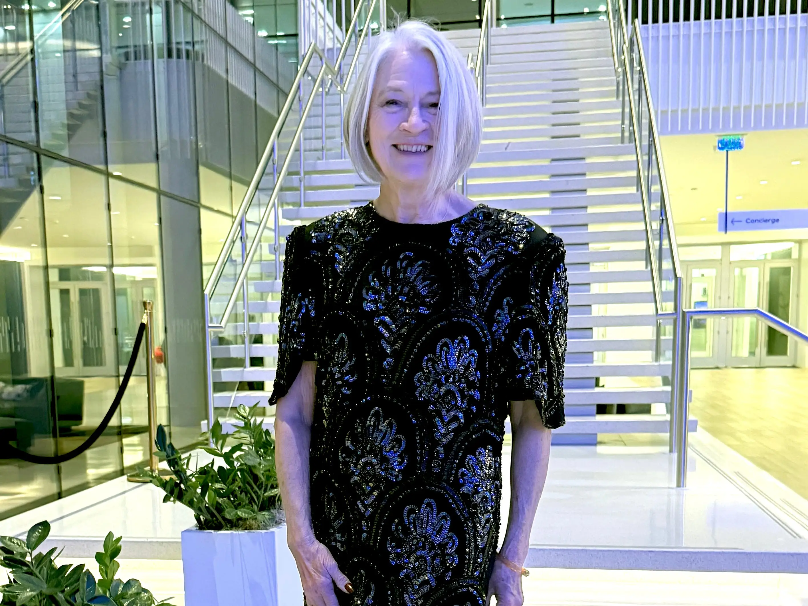 A woman in a black patterned dress standing in front of the stairs.