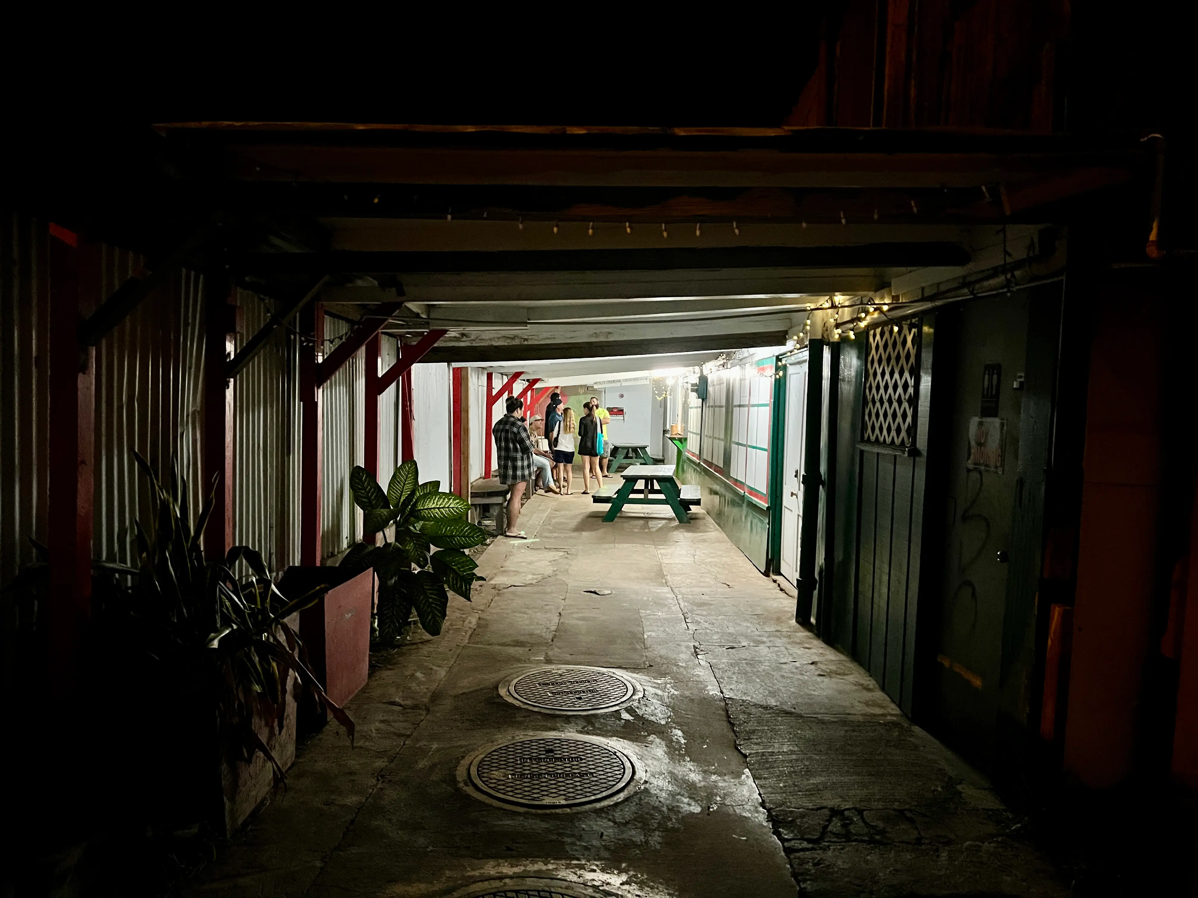 People waiting on line in well-lit hall area surrounded by dark