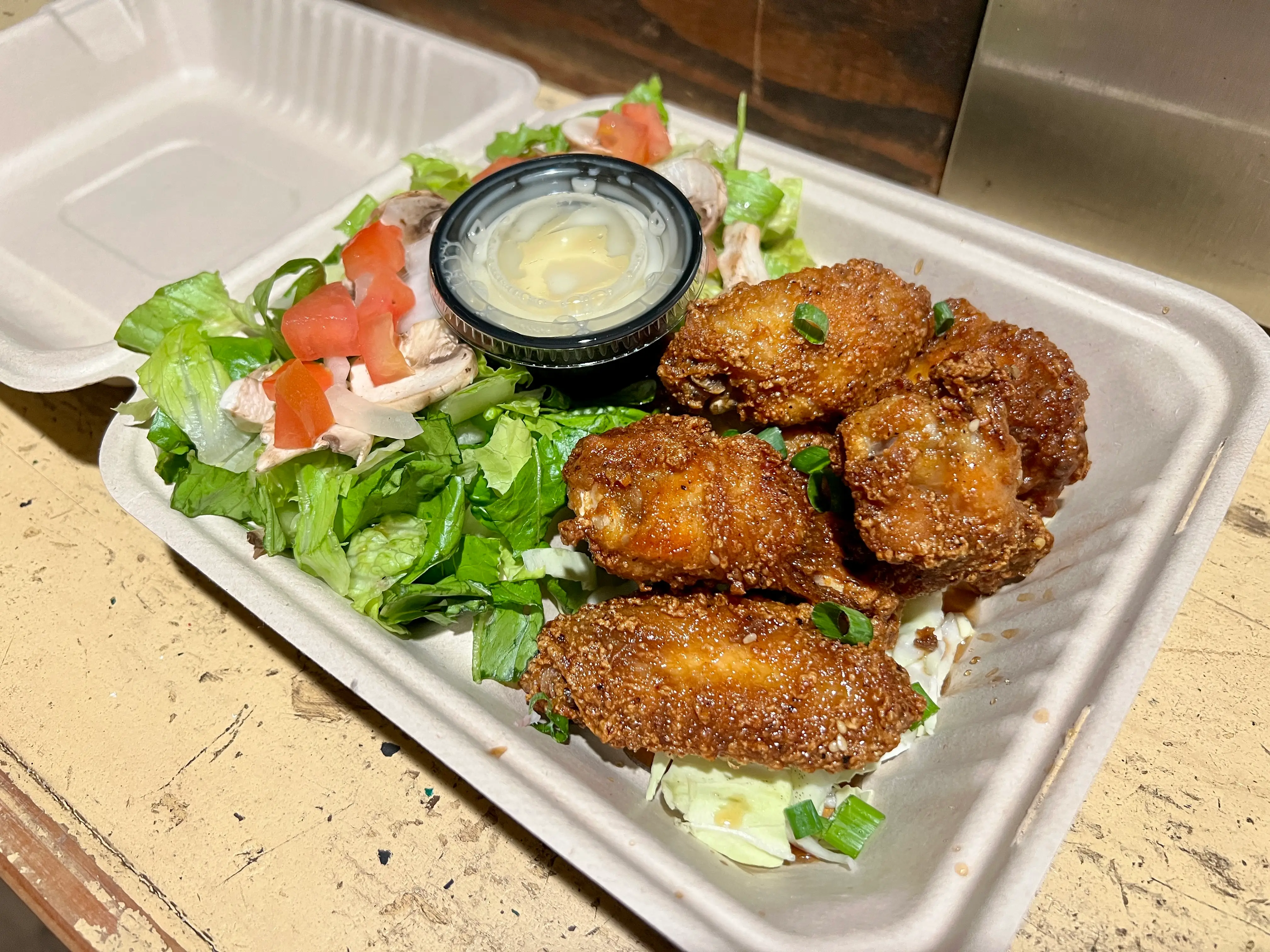 Korean chicken on bed of greens in takeout cointainer
