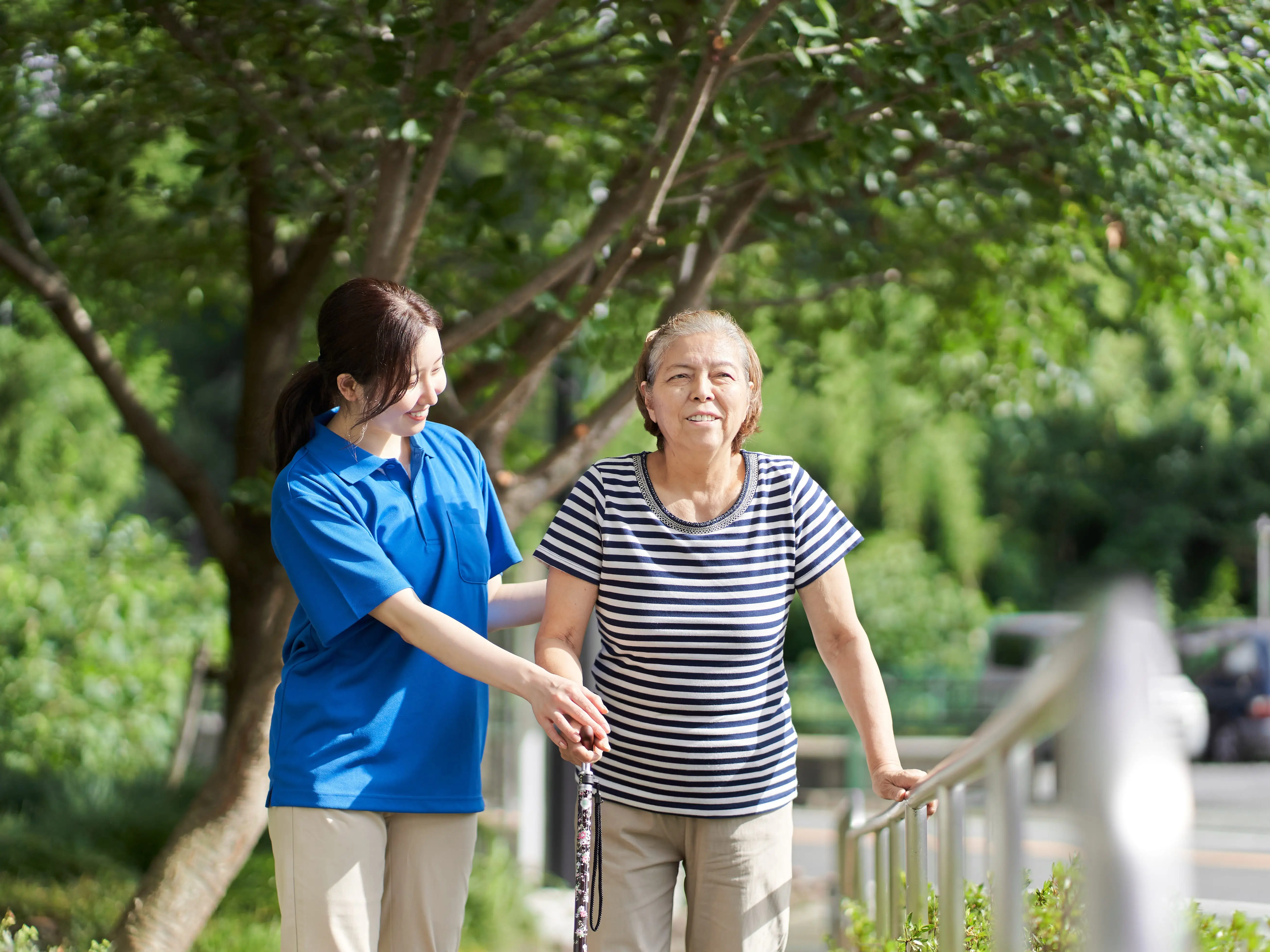 A healthcare worker or caregiver wearing a blue shirt is helping someone walk