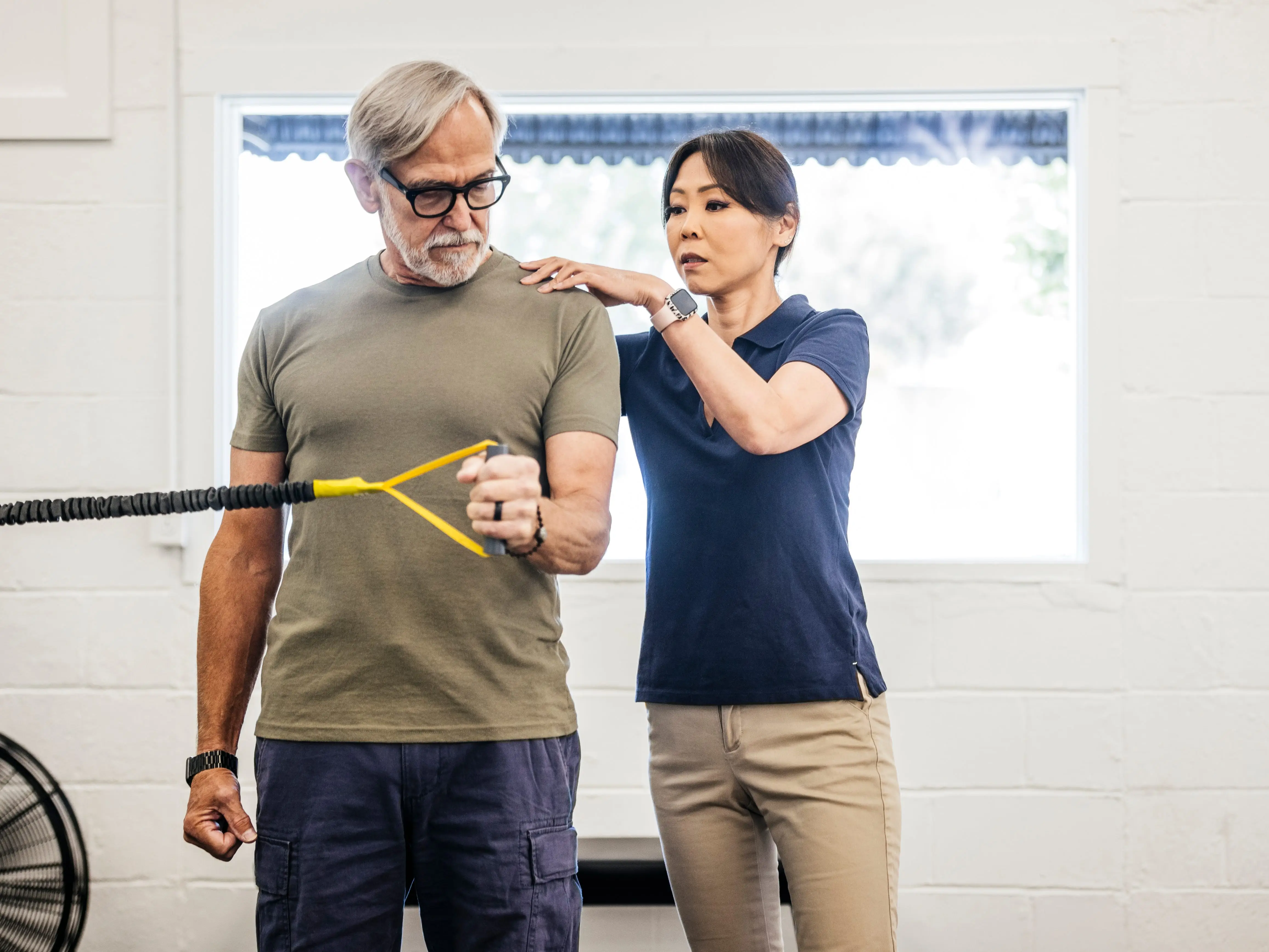 A man is doing physical therapy exercises with a stretch band while next to someone else