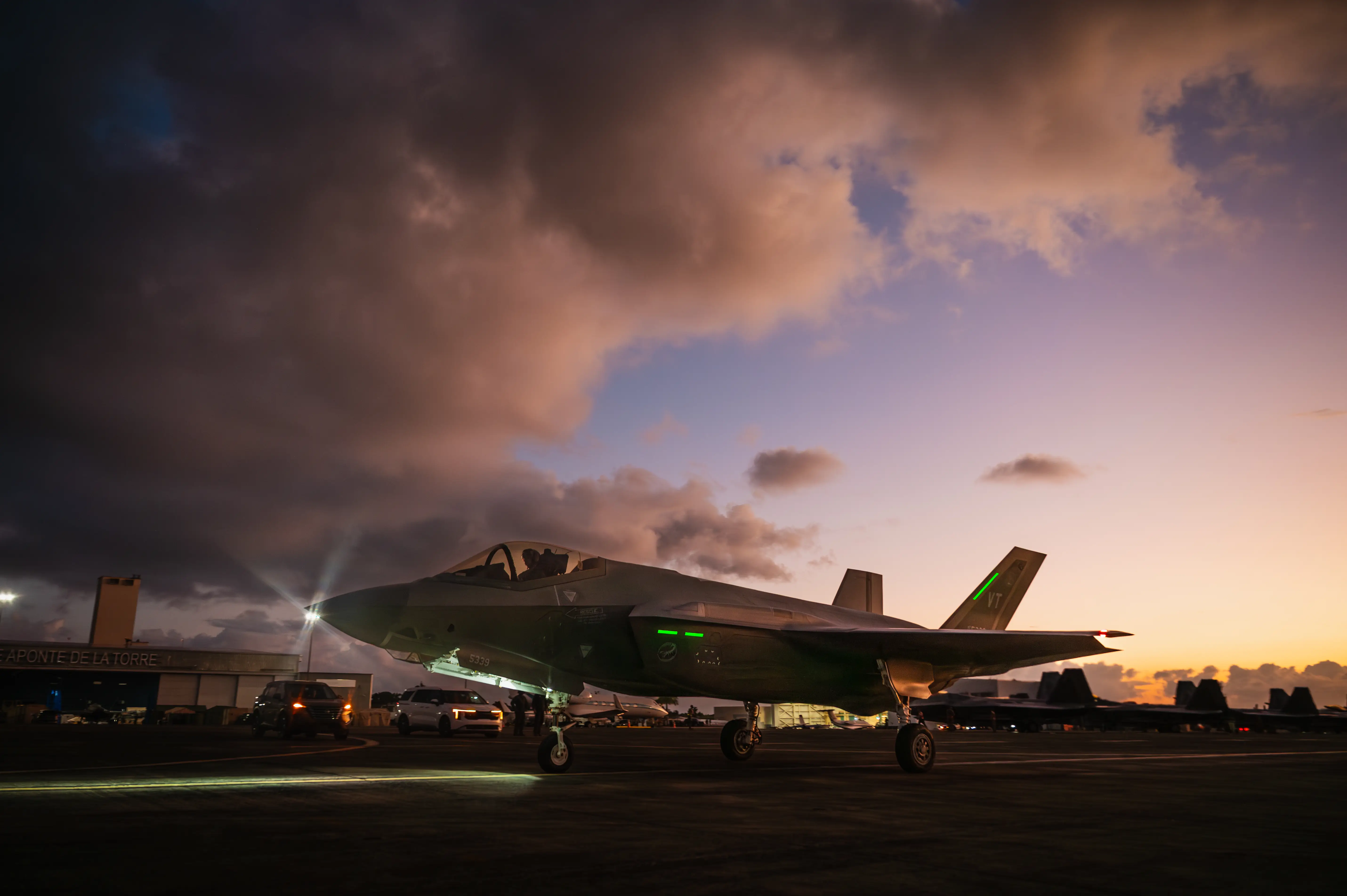 A US F-35 sits on the tarmac of an air base with a sun rise and cloudy sky in the background.