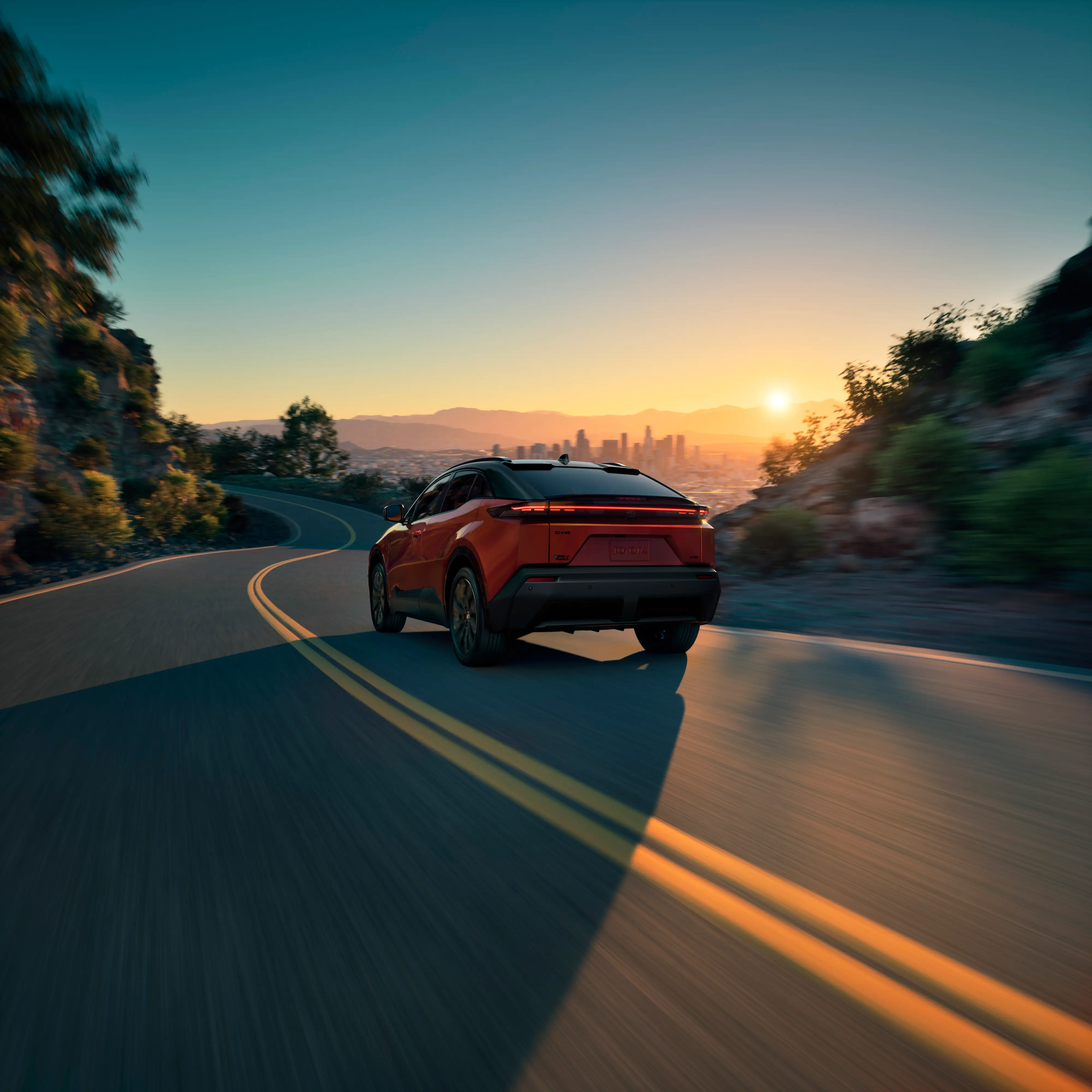 A red 2026 Toyota C-HR driving down a street at dawn.