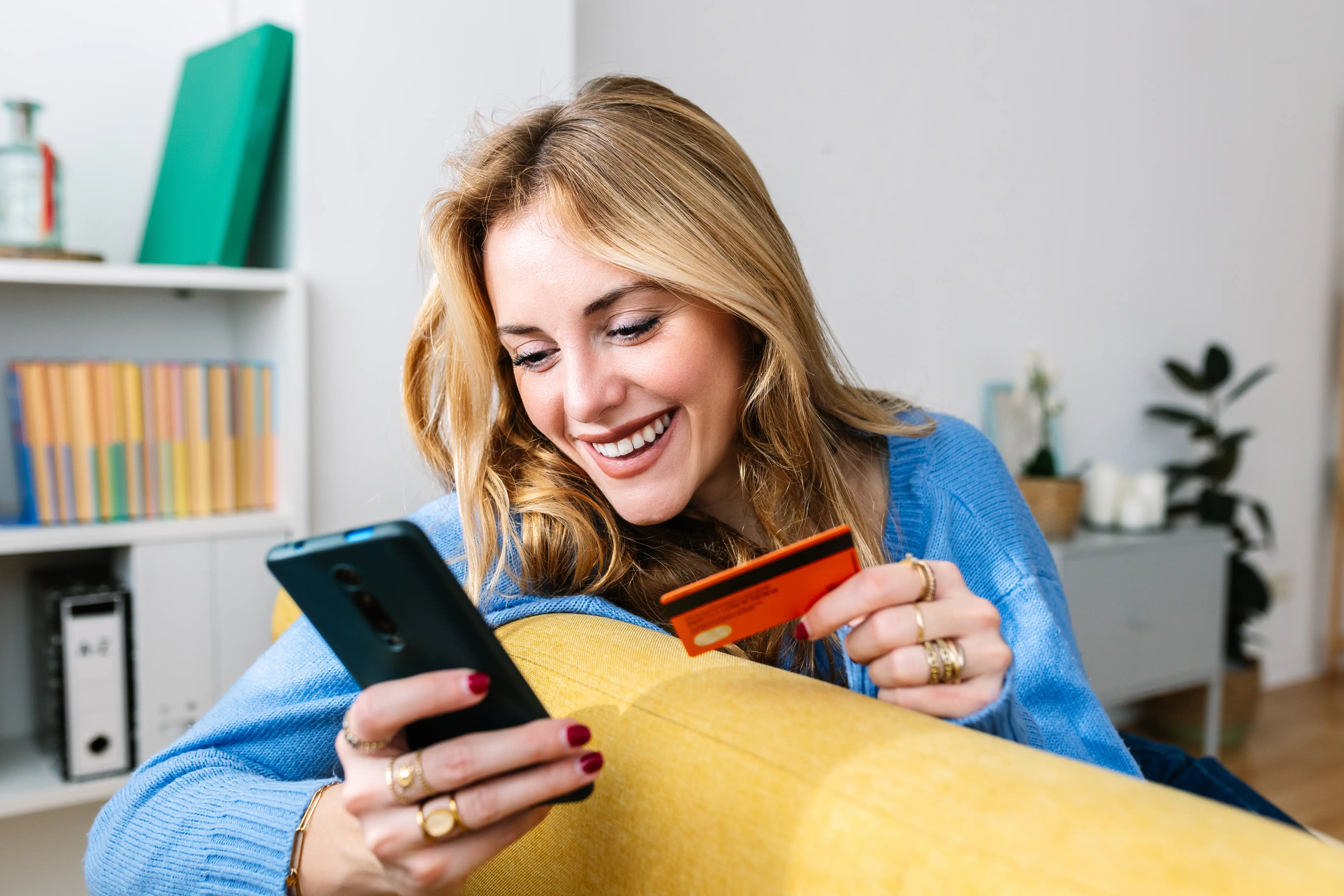 A young woman on her phone with a credit card in hand.