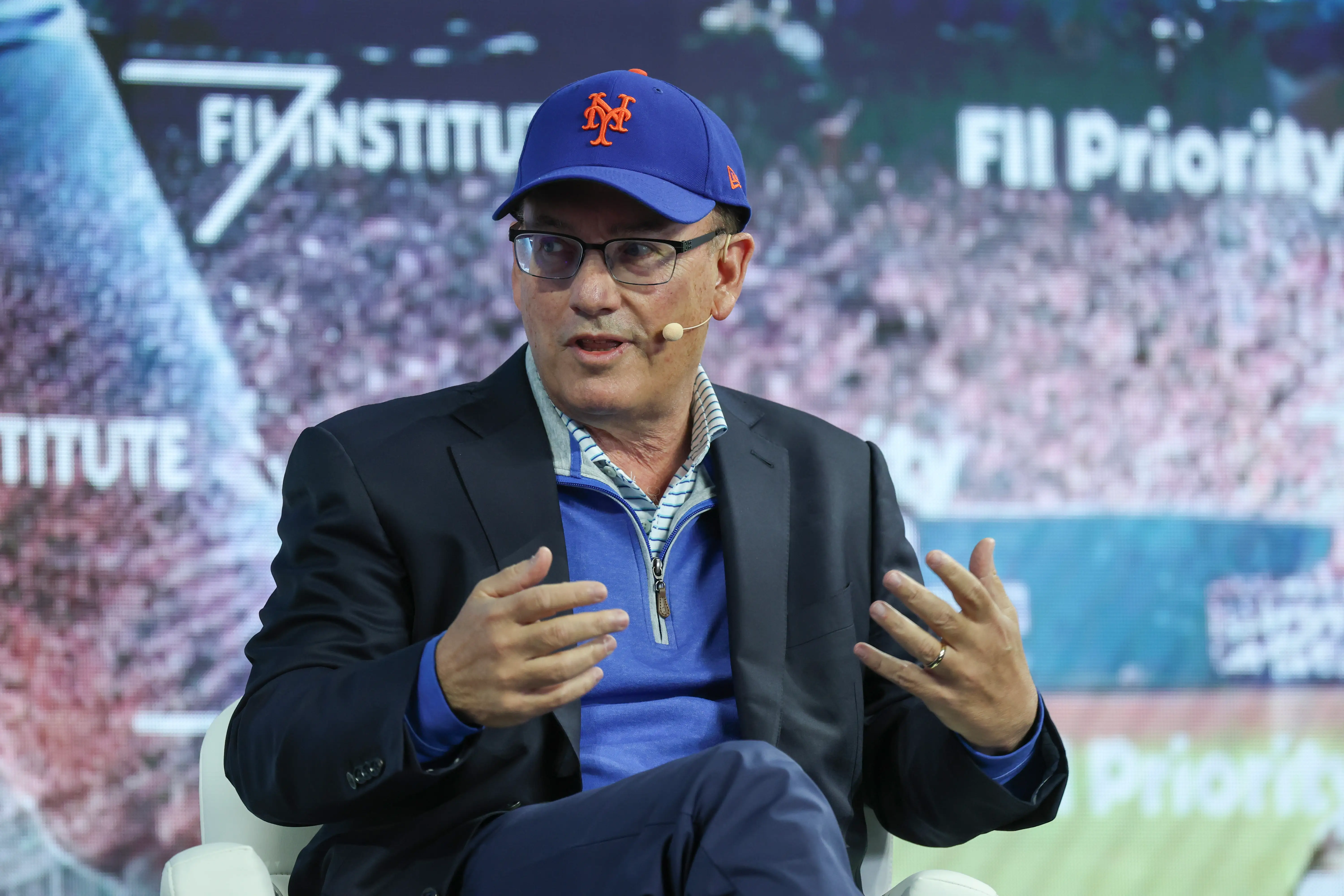 Steve Cohen talks on stage in a New York Mets hat