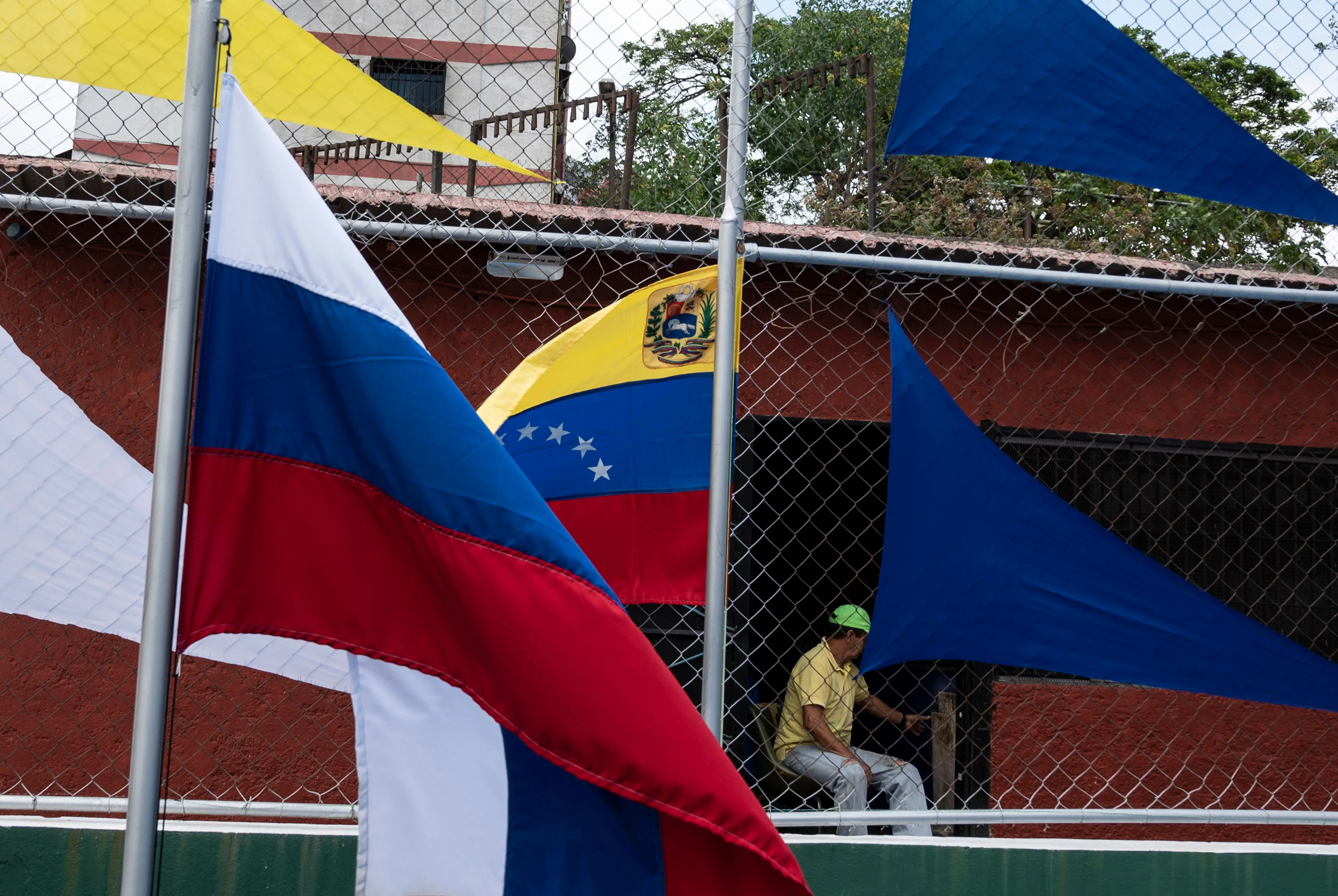 A man sits in front of the national flags of Russia (L) and Venezuela (R) waving in Caracas.