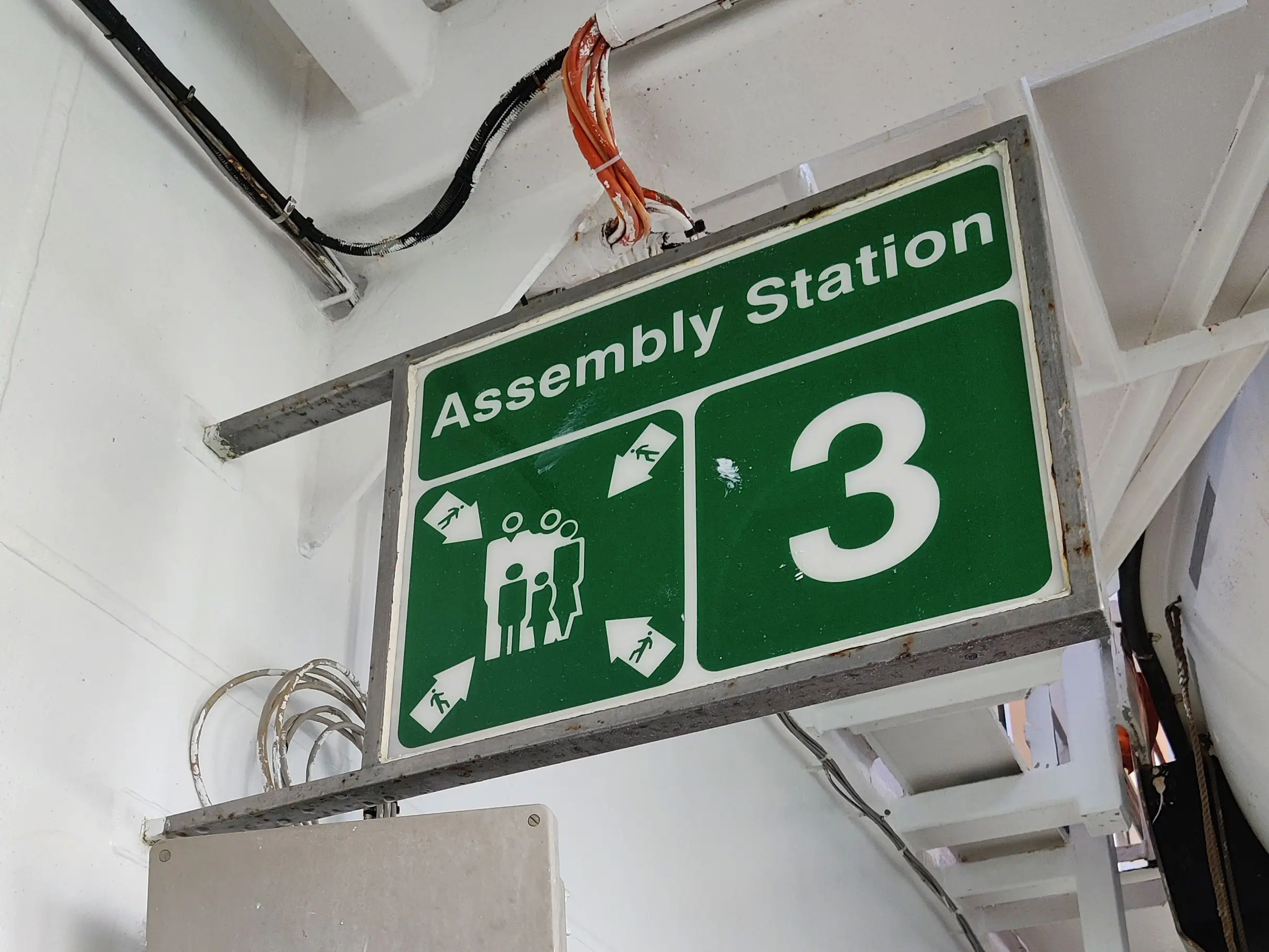 A green sign identifying the assembly station on a cruise ship.
