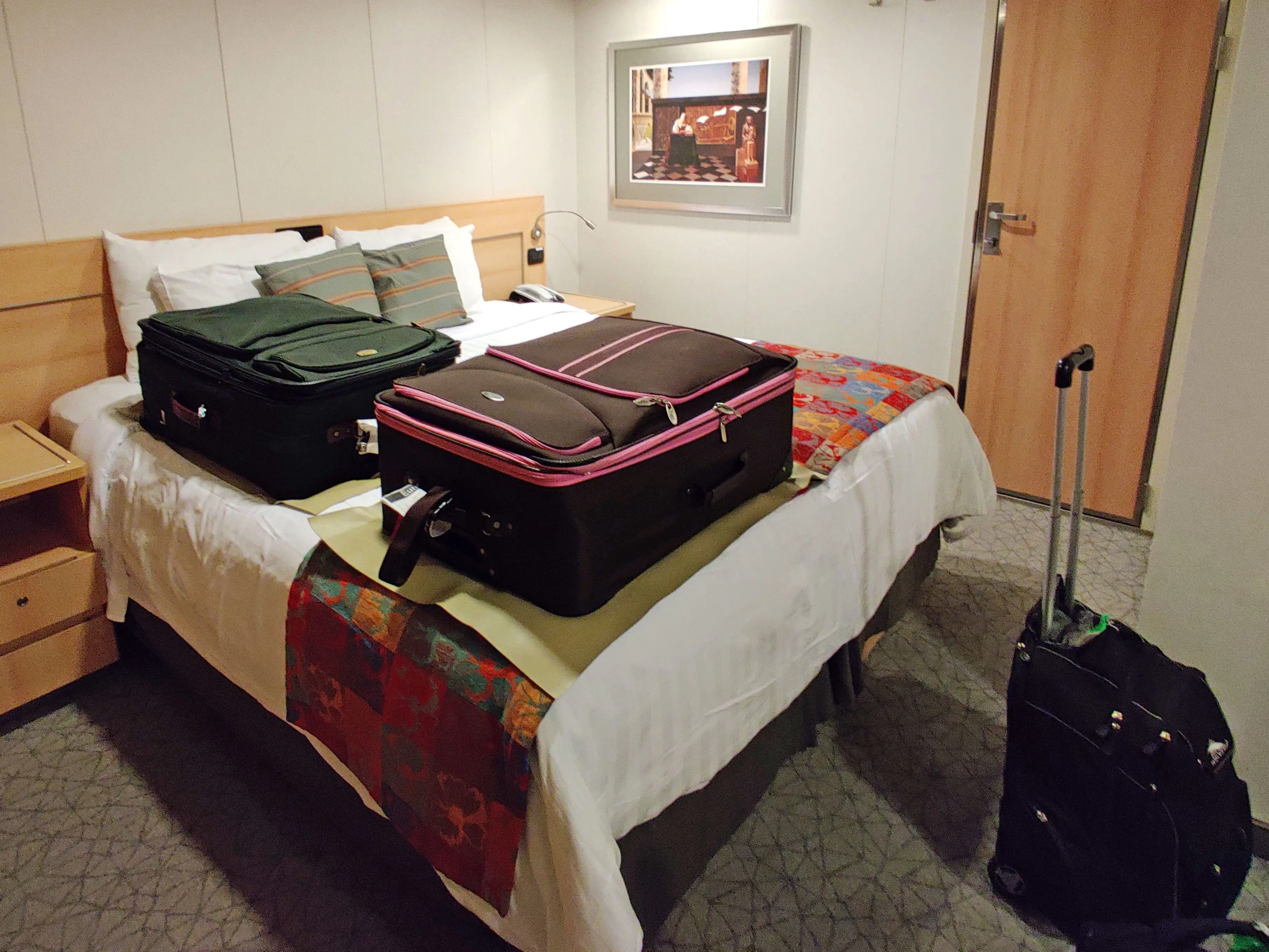 Suitcases on a bed and on the floor in a guest room on a cruise ship.