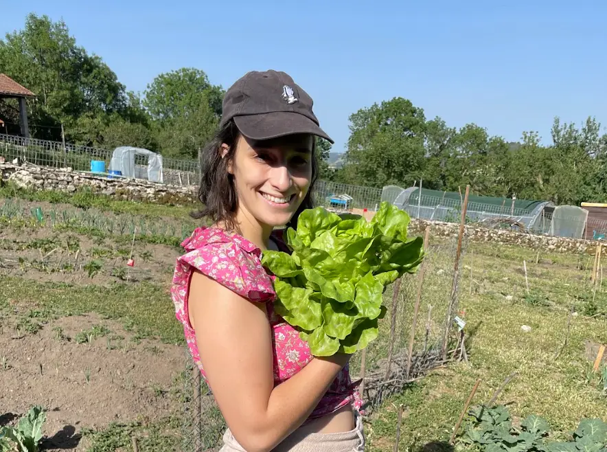 The writer standing outside, holding up lettuce she grew.