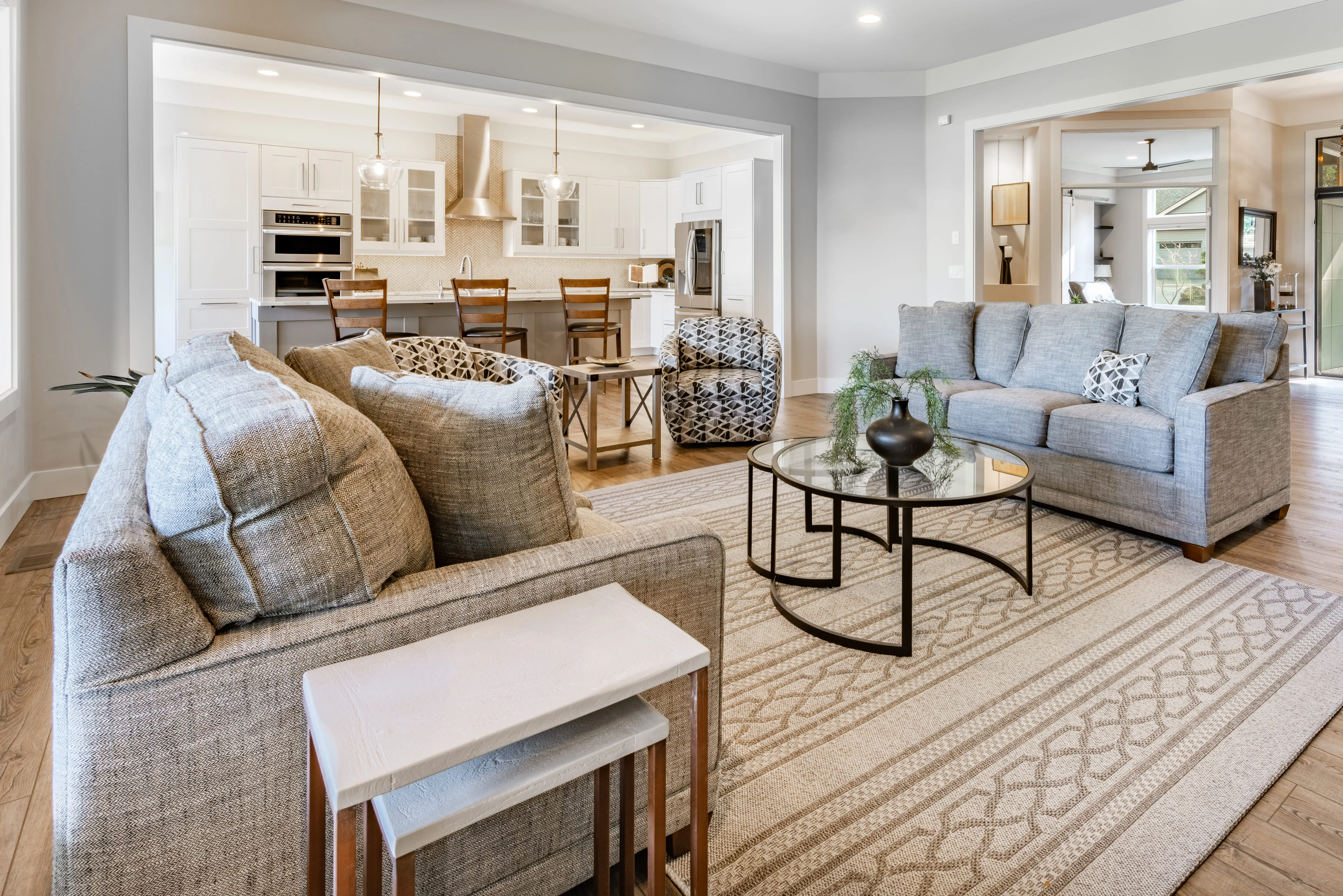Living room with gray couch on edge of beige rug, ceiling fan, overhead lighting