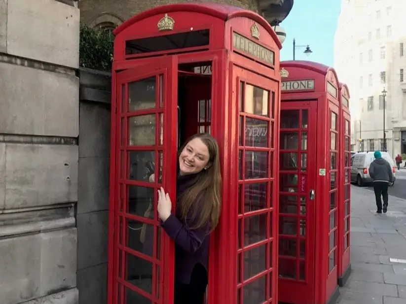Woman peeking out of red phone booth, smiling