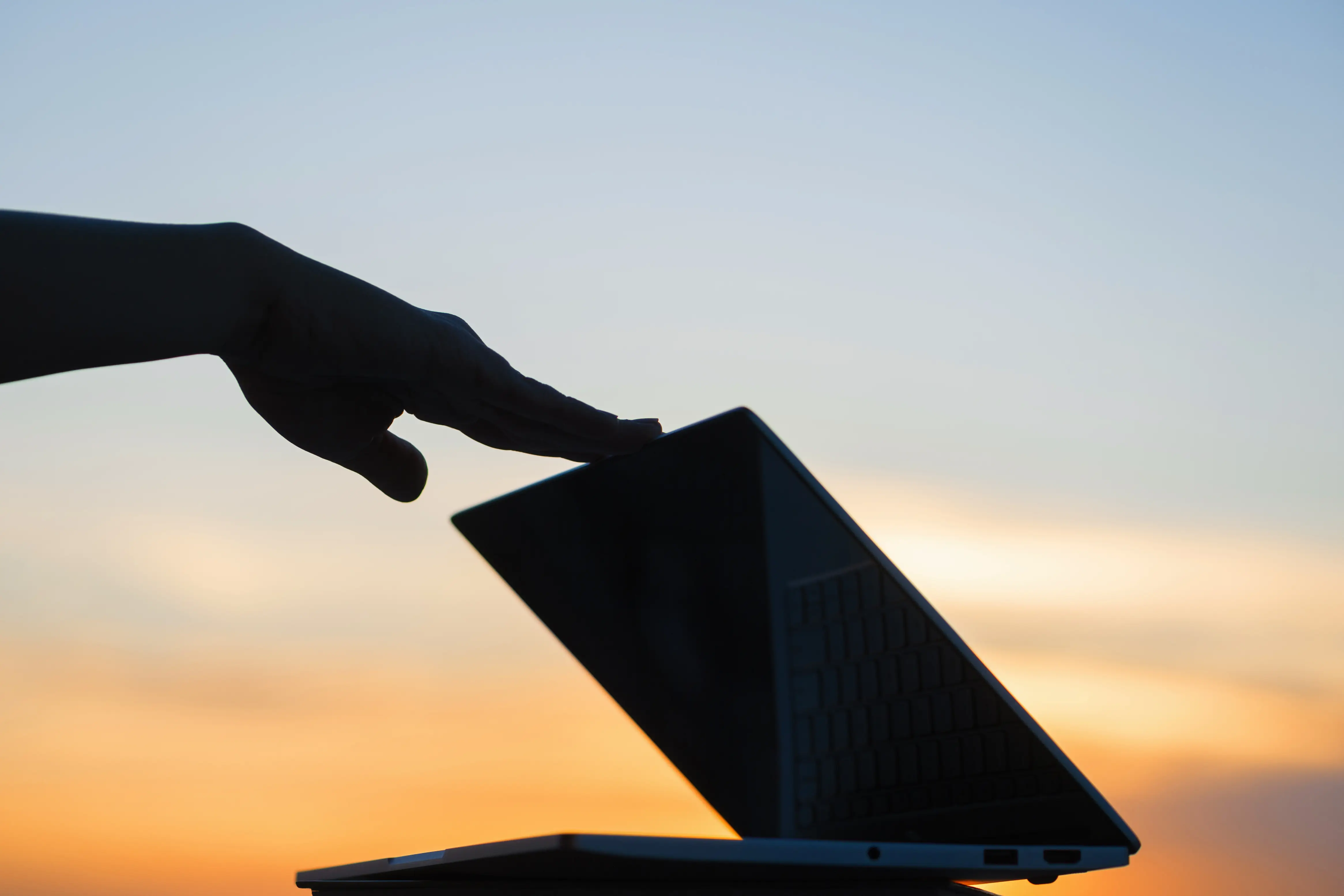 Person closing laptop at sunset