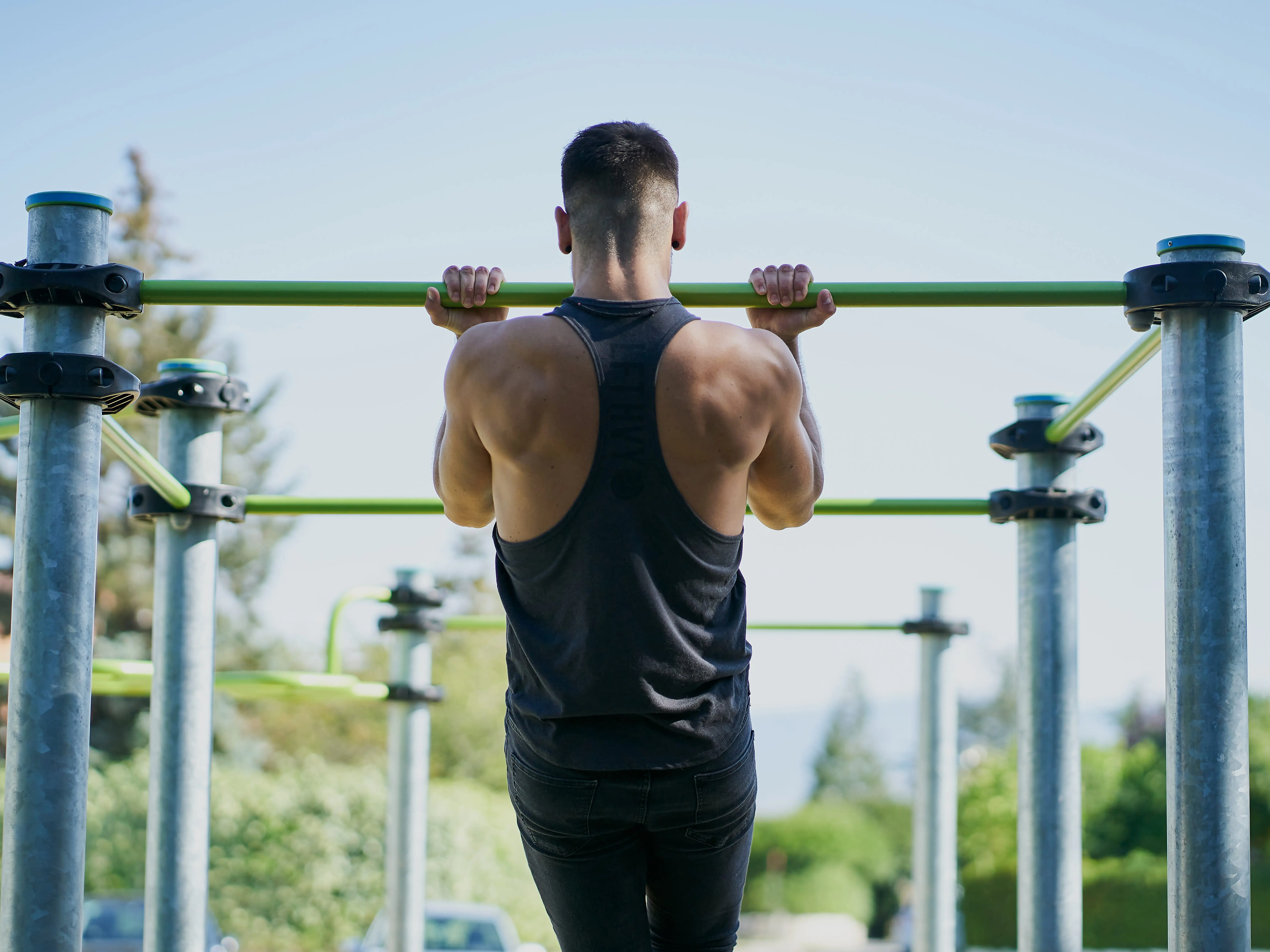 A man does chin-ups at an outdoor gym.