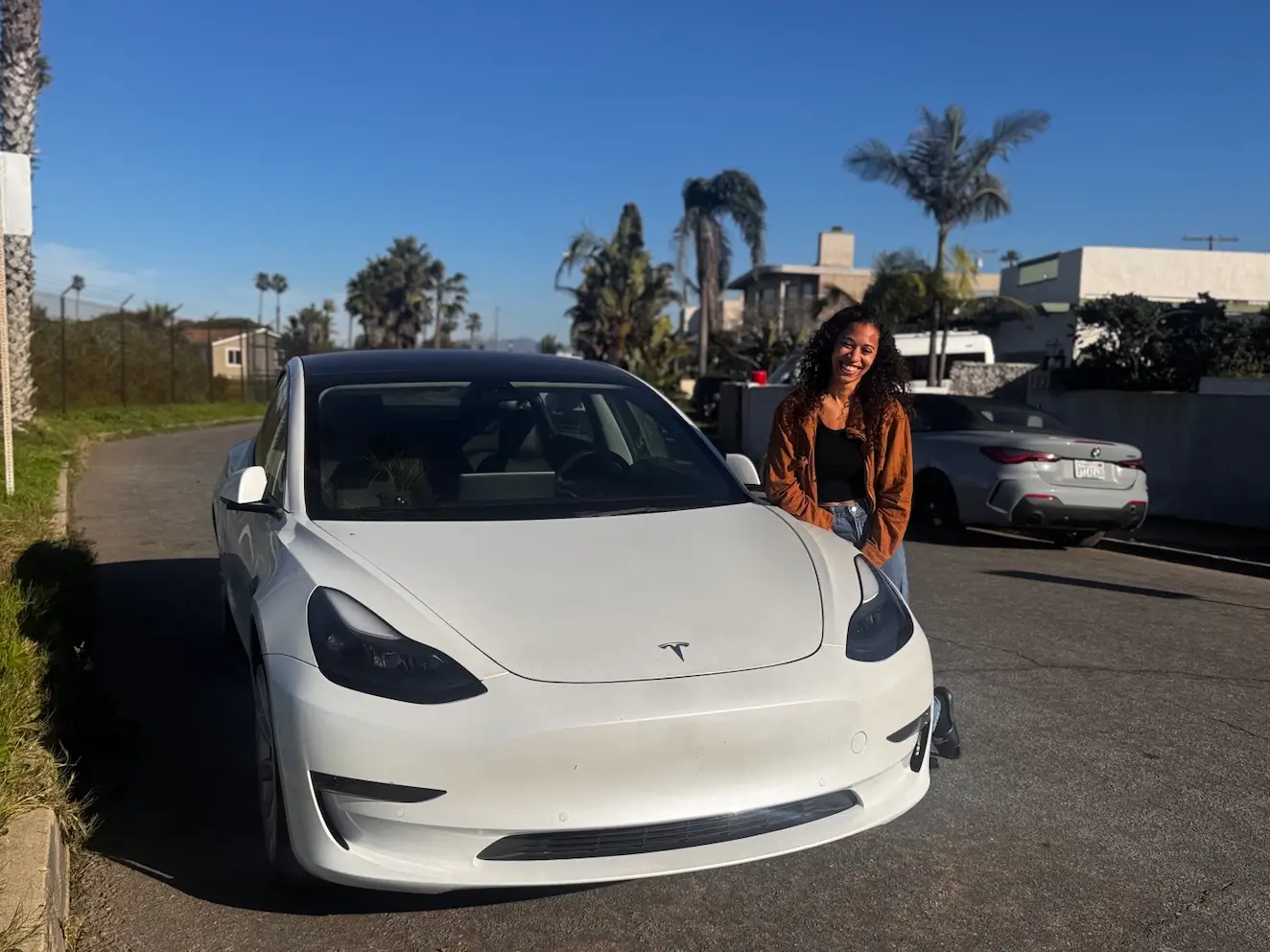 A white Tesla Model 3 sedan parked on the side of the road in California with Leslie Snipes, the owner, leaning against the car.
