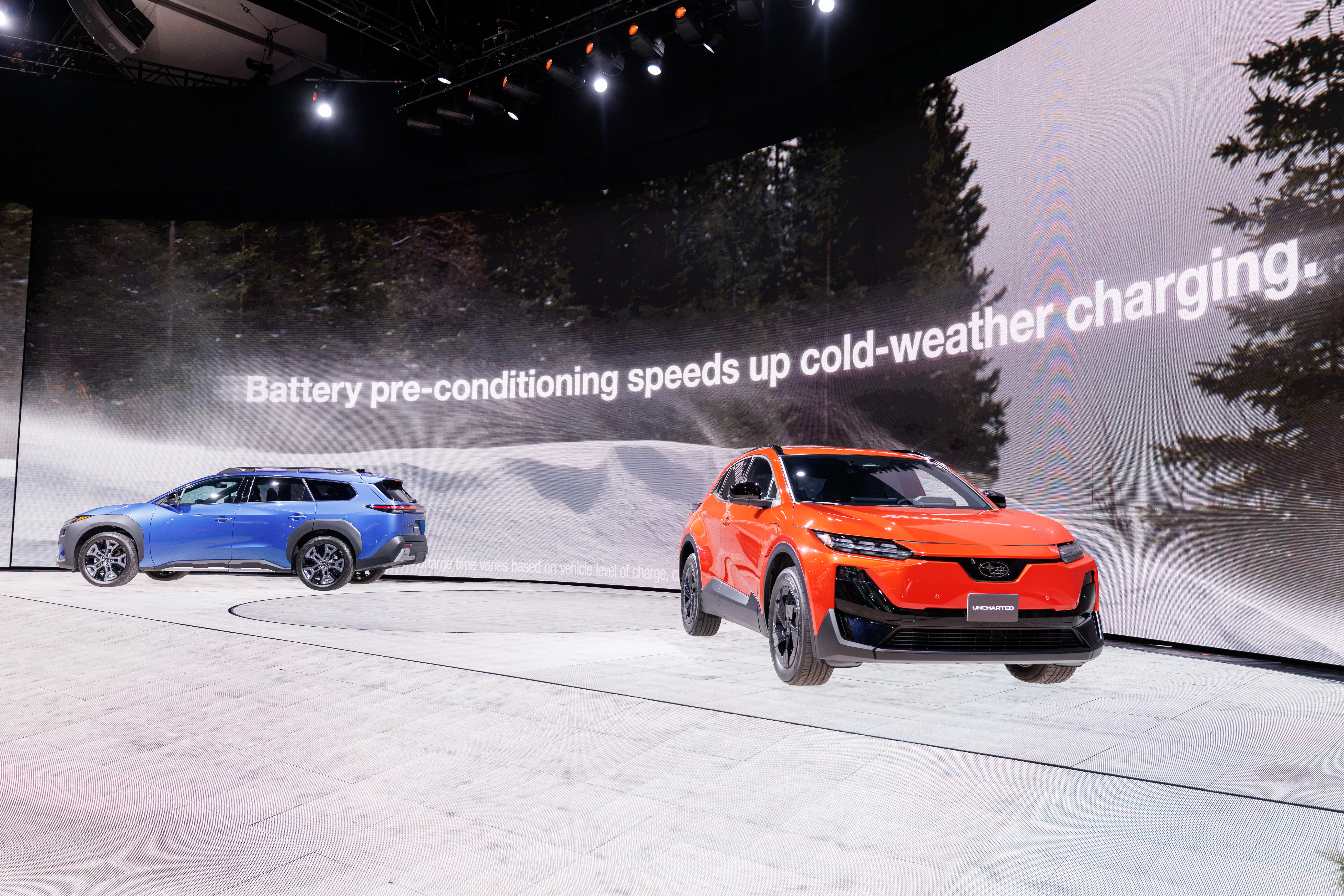 Two Subaru EVs, a red-orange Uncharted SUV and a blue Trailseeker wagon, are parked on a white stage during the LA Auto show.