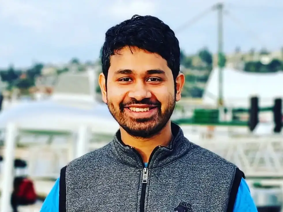 headshot of a man in a vest and blue tshirt