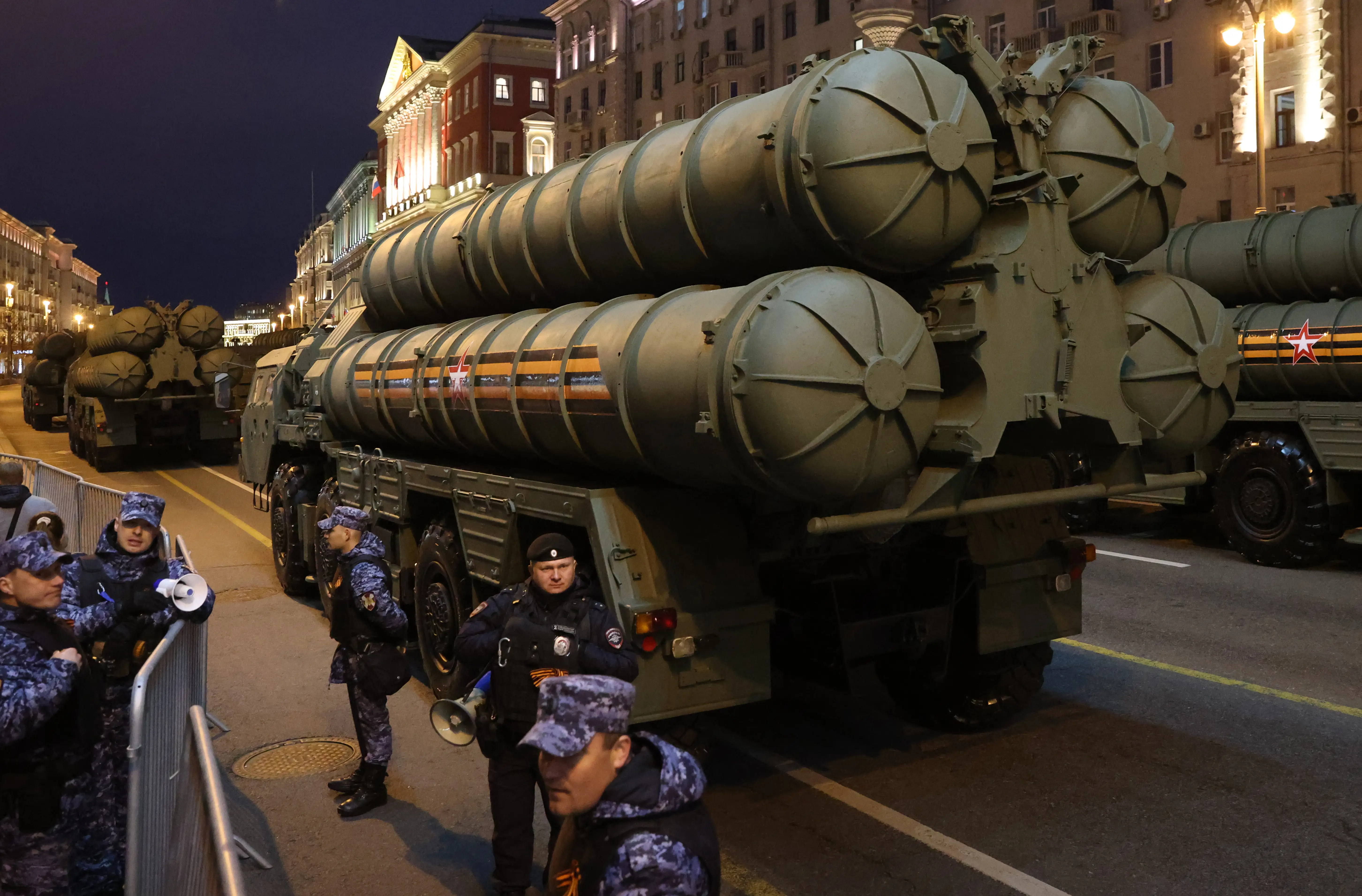 A large green air defense system on a city road at night with figures in blue camouflage standing beside it