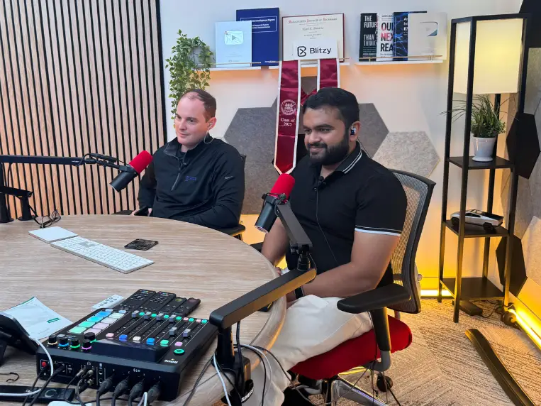 Pardeshi and his co-founder Brian Elliott sitting at a table in a podcast studio. There are red microphones in front of them.