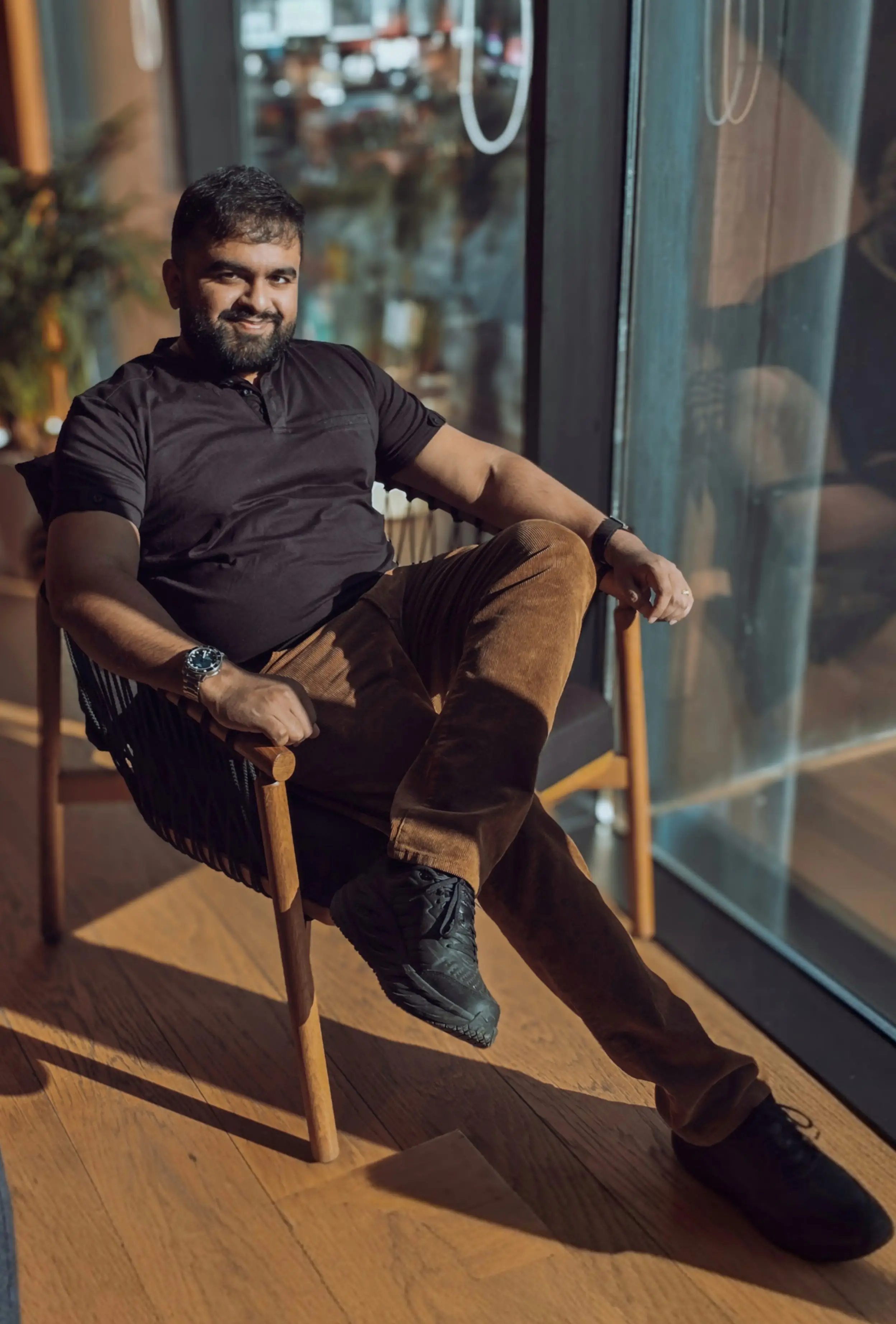 Pardeshi is sitting cross-legged on a wooden chair.