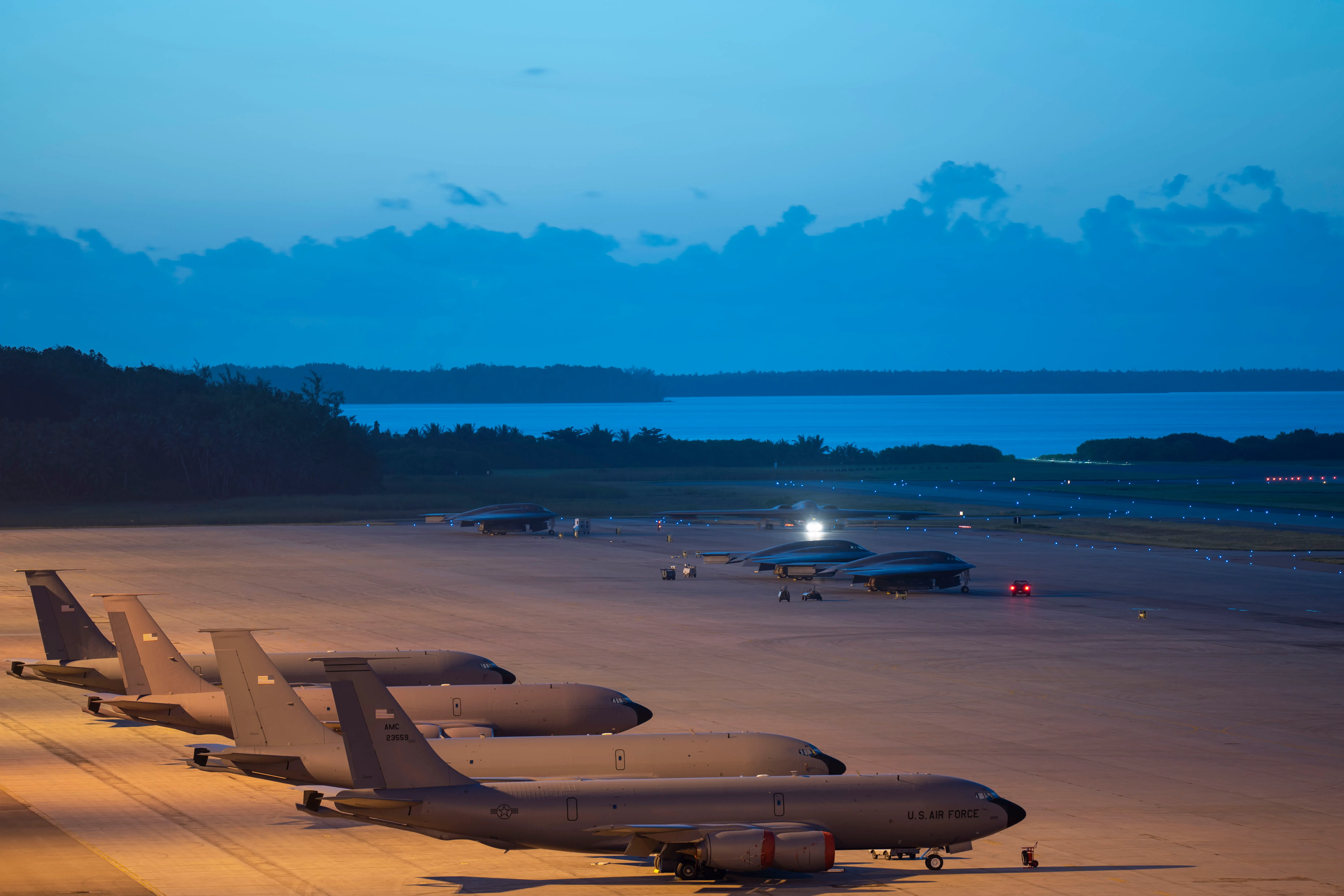 US Air Force B-2 bombers and KC-135 Stratotanker aircraft sit on a tarmac with the view of the ocean and sky in the background.