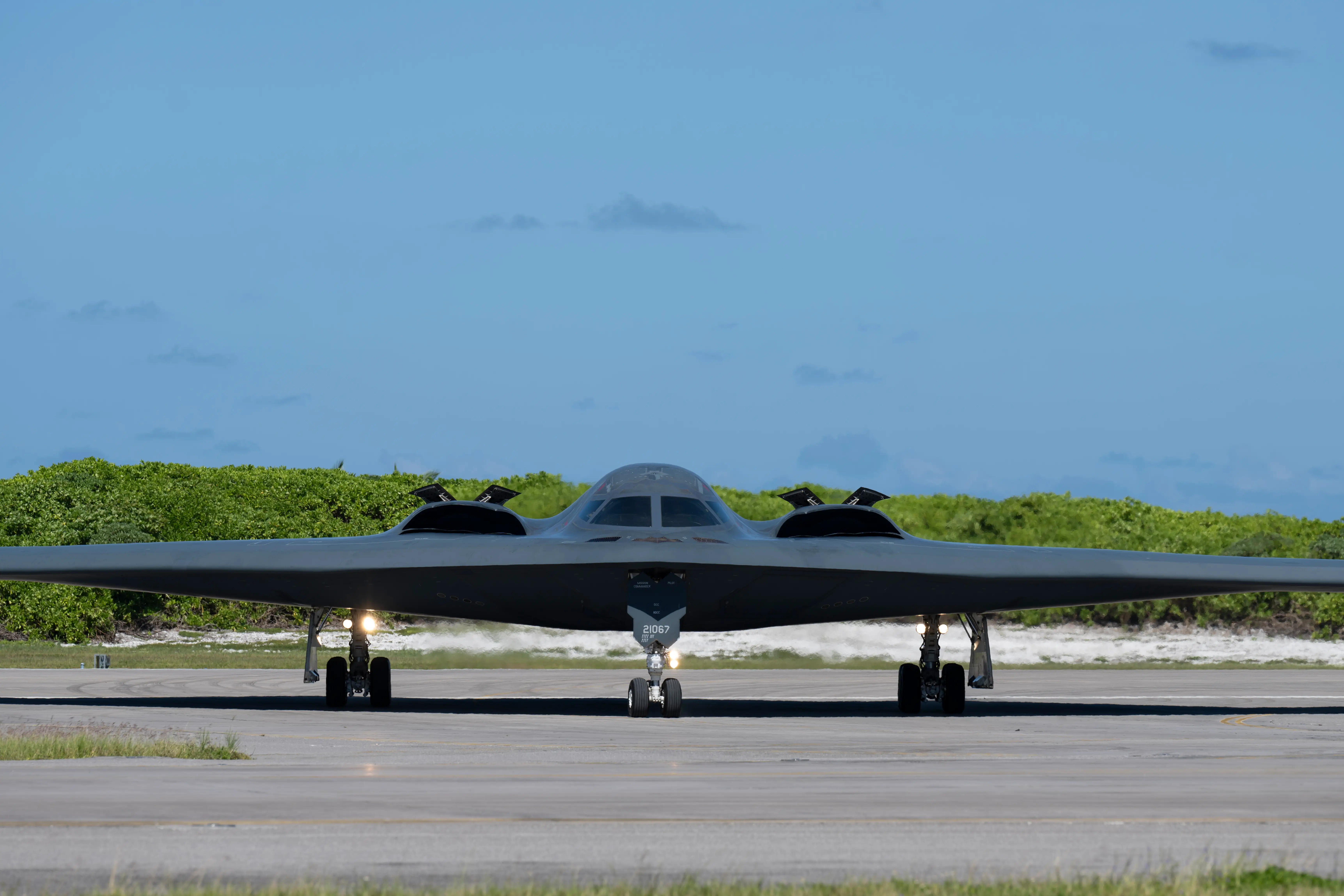 A US Air Force B-2 bomber sits on tarmac with a blue sky in the background.
